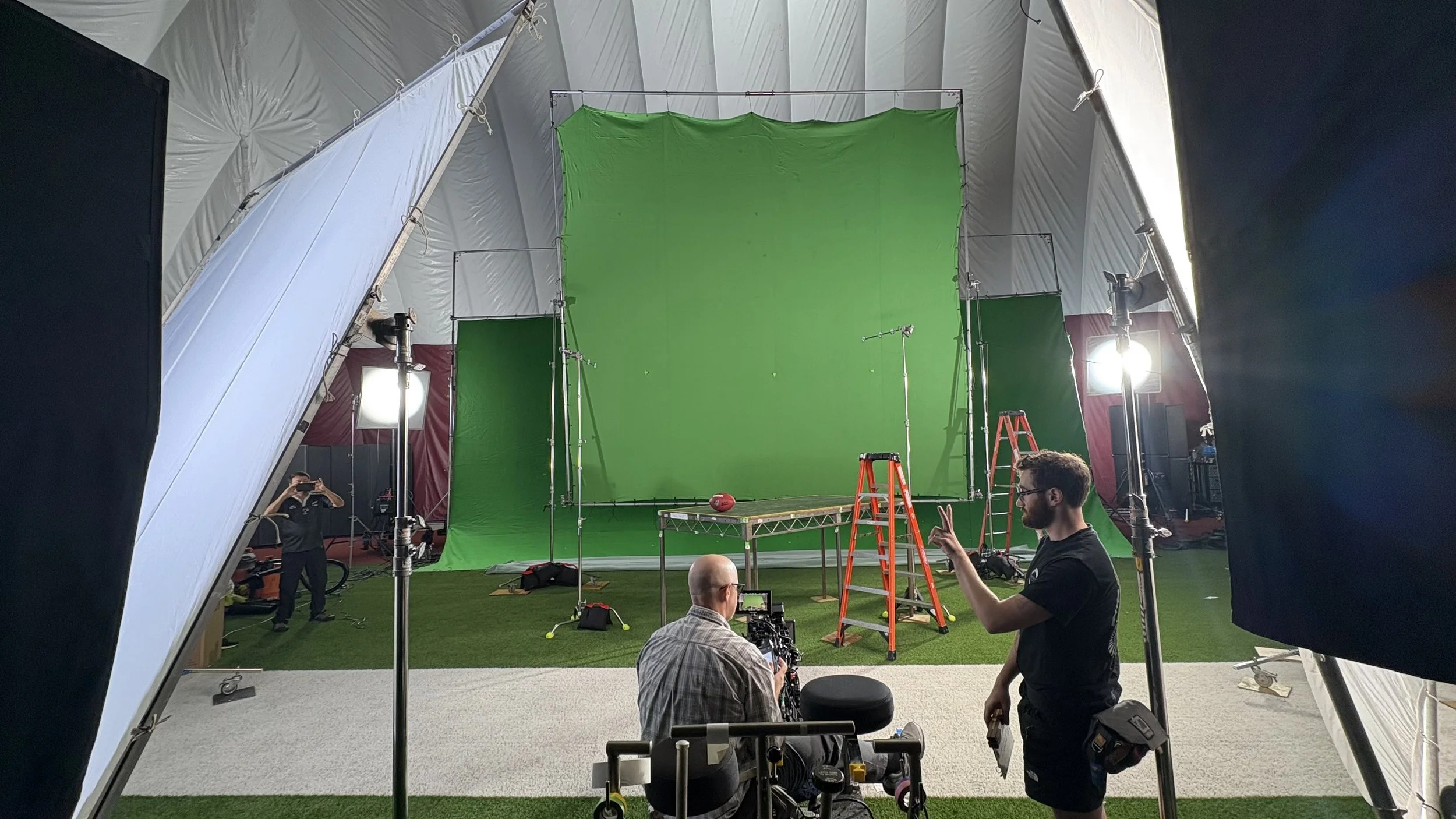 "Washington Commanders" Netflix Special: 
Green screen 20x20 built, several crew members set up filming equipment, including multiple lights, a green backdrop, ladders, and cameras.