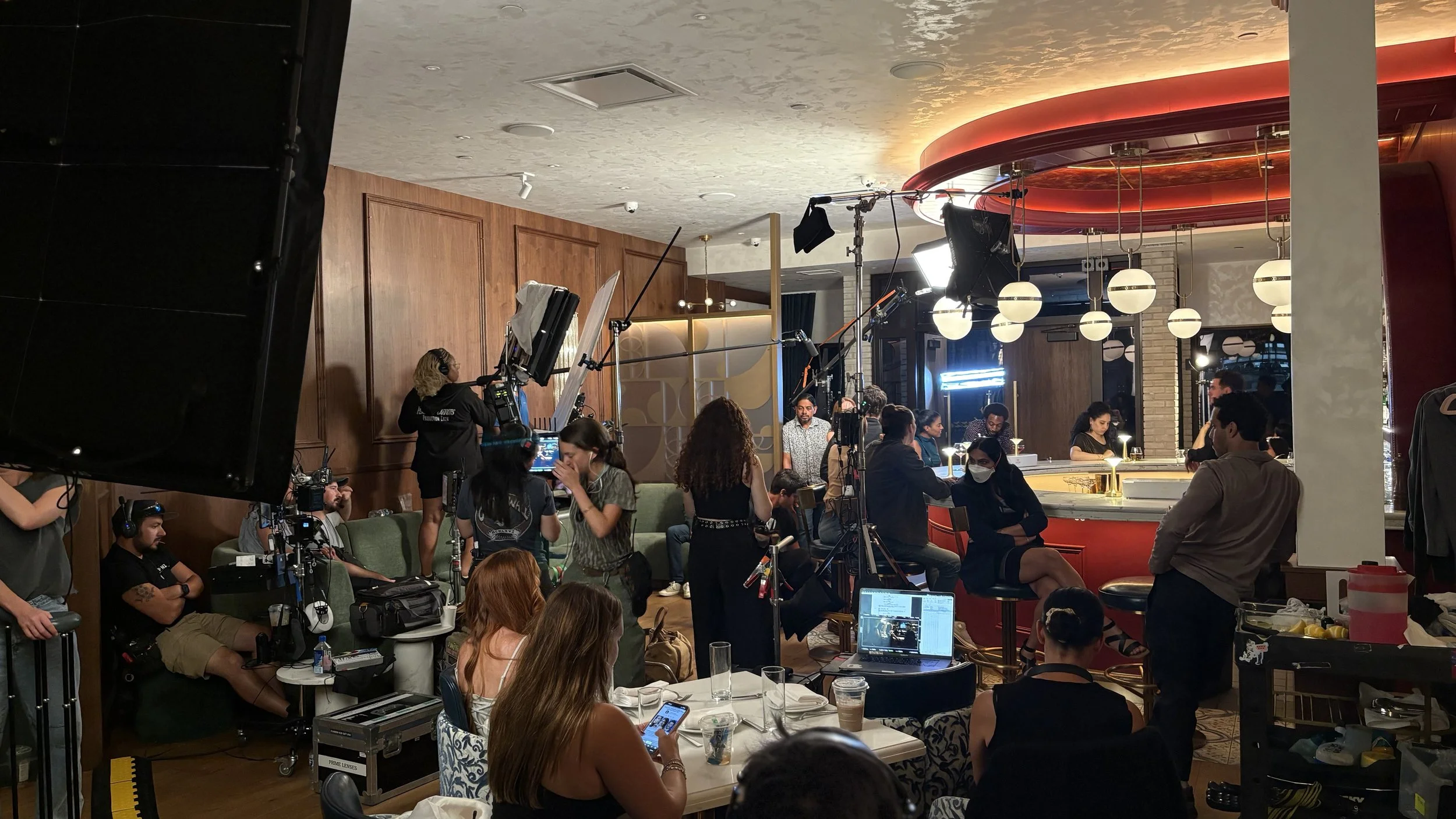 A busy filming set inside a restaurant with crew members, cameras, lighting equipment, and actors preparing for a scene. Key Grip - Feature Film "Run"