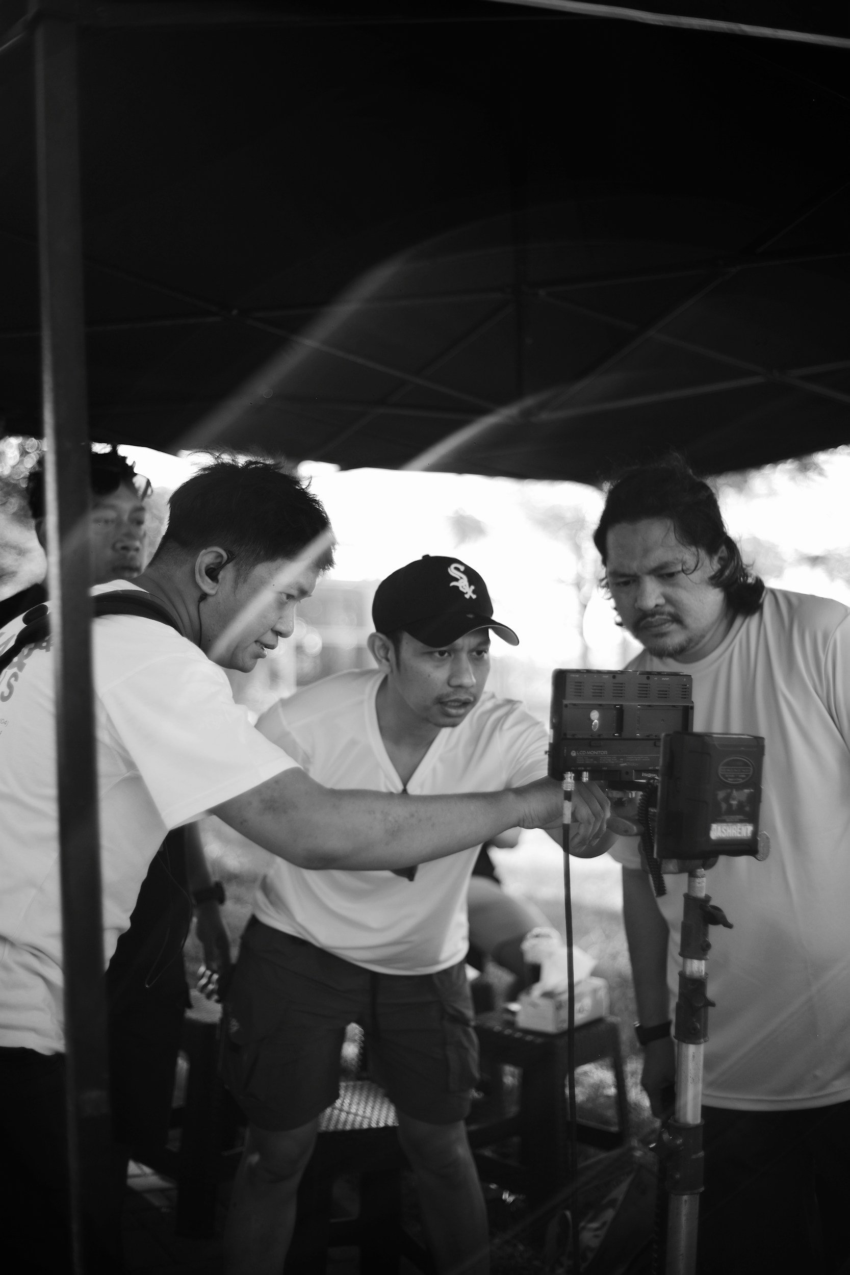 Three filmmakers gathered around a monitor on set, reviewing footage together during a production shoot.