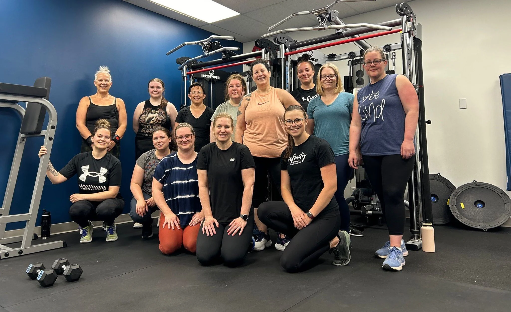 Group of women in a gym, smiling, with workout equipment around them.