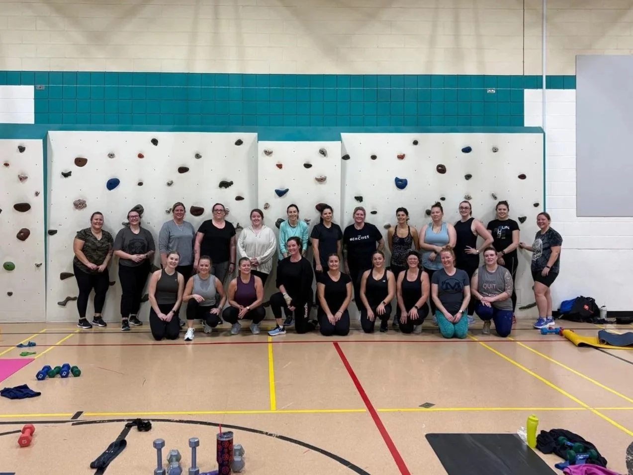 Group of women posing in front of an indoor rock climbing wall inside a gymnasium.