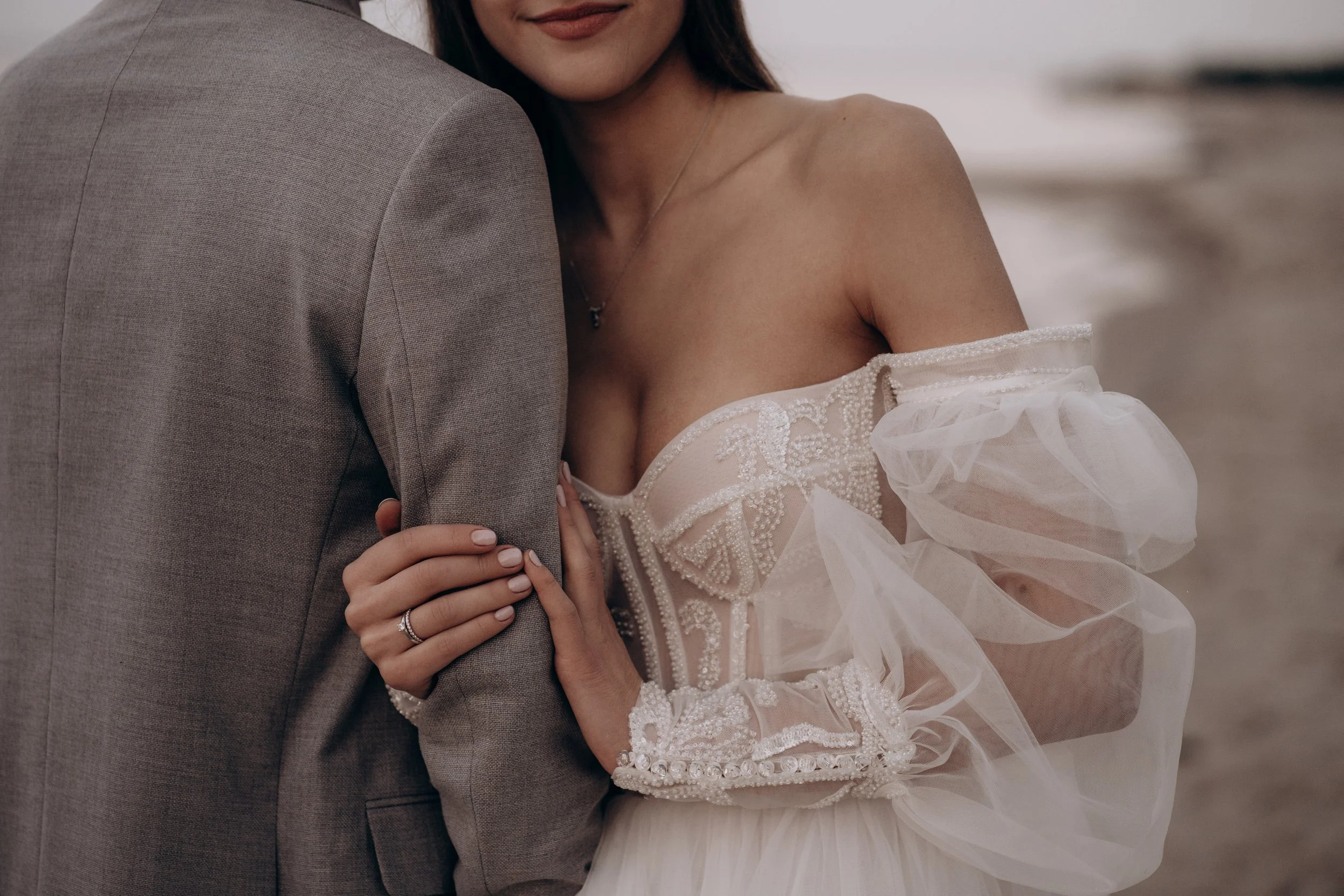 Close-up of a bride and groom embracing, focusing on the bride's face, shoulders, and wedding dress, with the groom wearing a light gray suit.