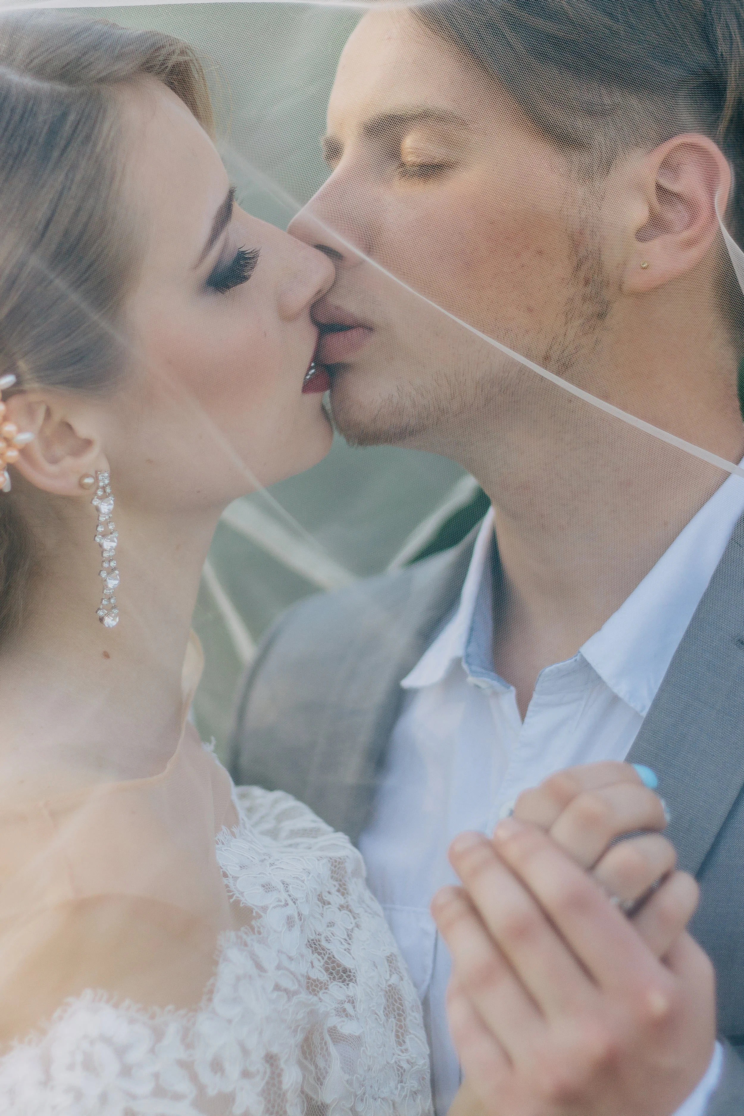 A bride and groom sharing a kiss through a wedding veil during their wedding ceremony, holding hands closely.