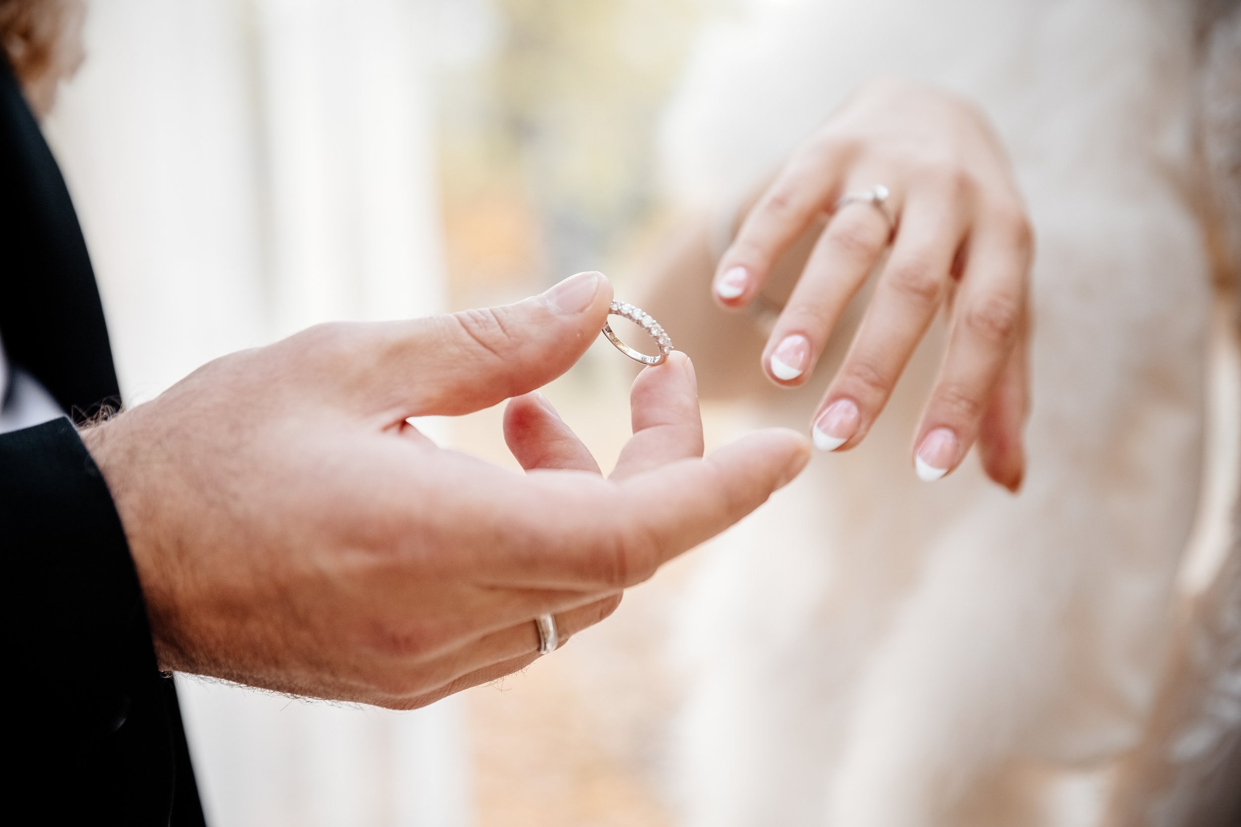 Close-up of a person presenting a diamond wedding ring to another person's hand.