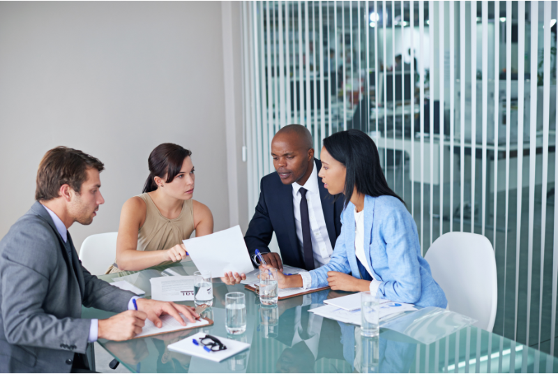 A group of professionals in a formal office setting discussing documents during a decision making meeting under pressure.