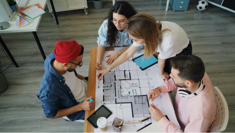Four people reviewing a building floor plan at a table in a modern office.