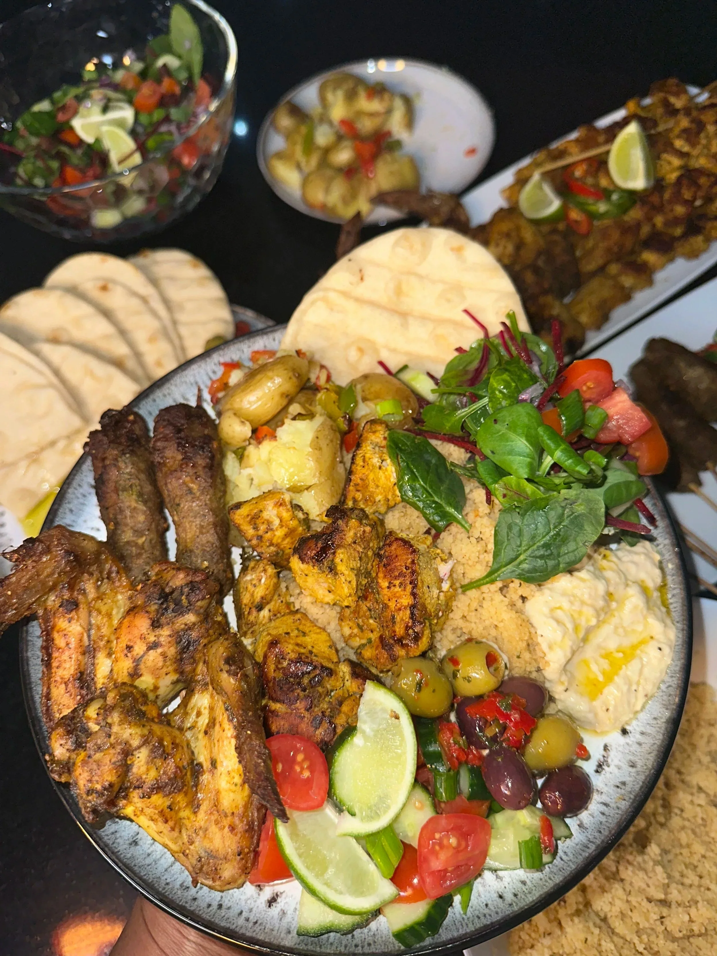 A large plate with various grilled meats, rice, fresh salad with cucumbers, cherry tomatoes, and black olives, and slices of lime.
