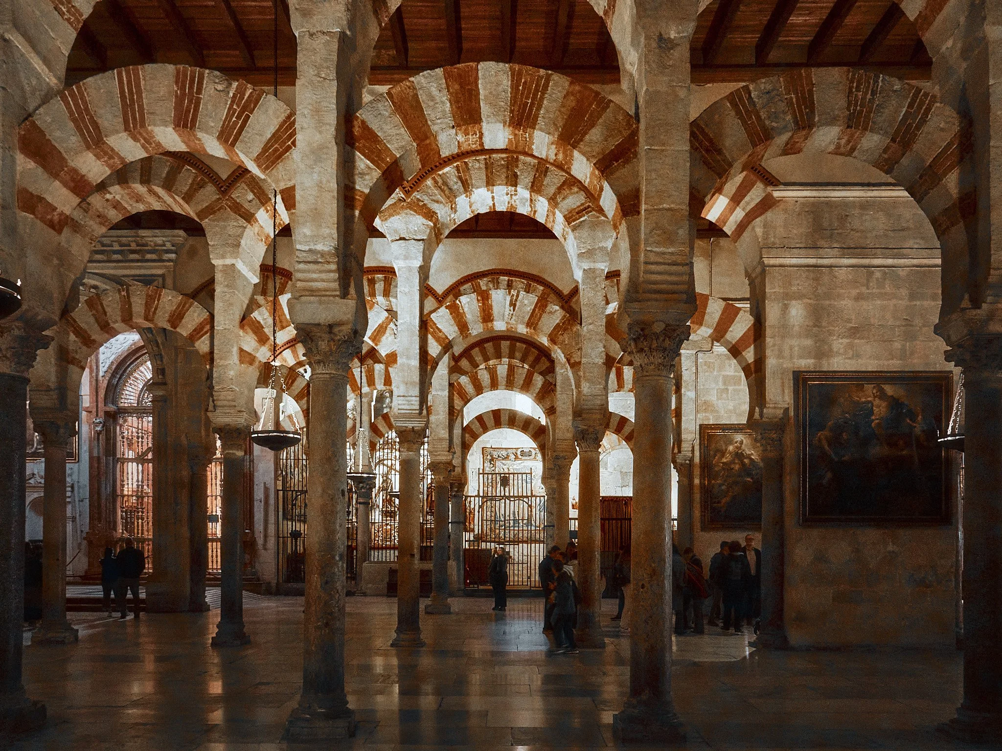 Interior de una iglesia o catedral con arcos de medio punto y columnas de piedra, con un grupo de personas observando las obras en las paredes.