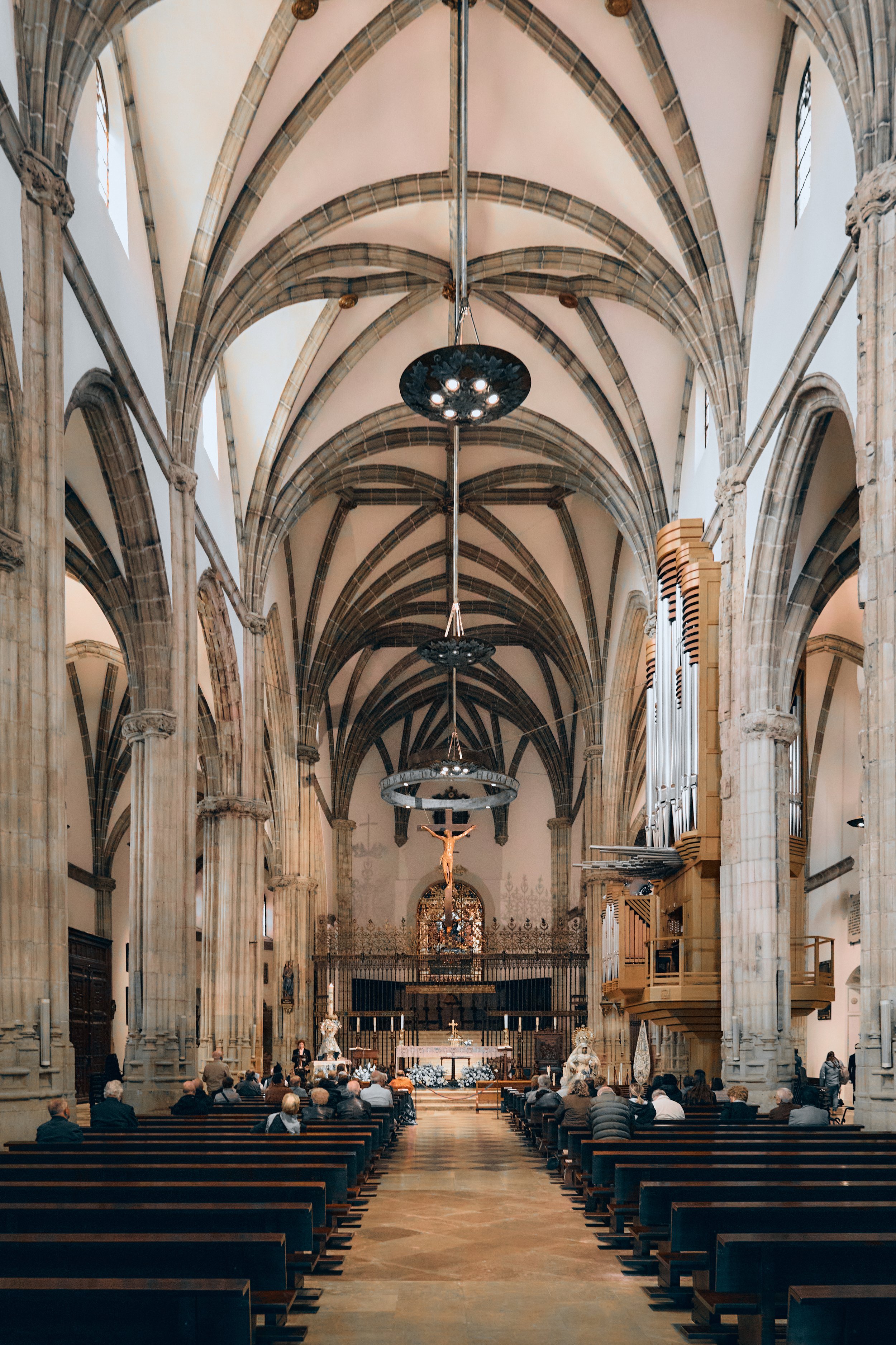 Interior de una iglesia con arcos góticos, bancos y una cruz en el altar.