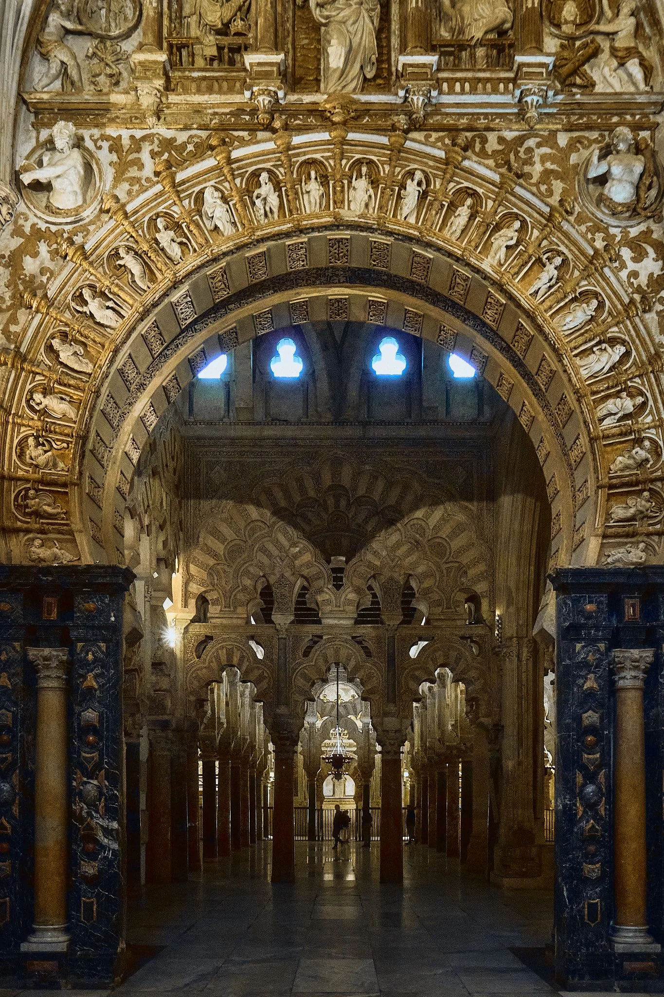 Arco decorado en una iglesia con relieves y columnas de piedra, con luz natural entrando por pequeñas ventanas en el techo. Interior de un templo con columnas altas y un altar al fondo.