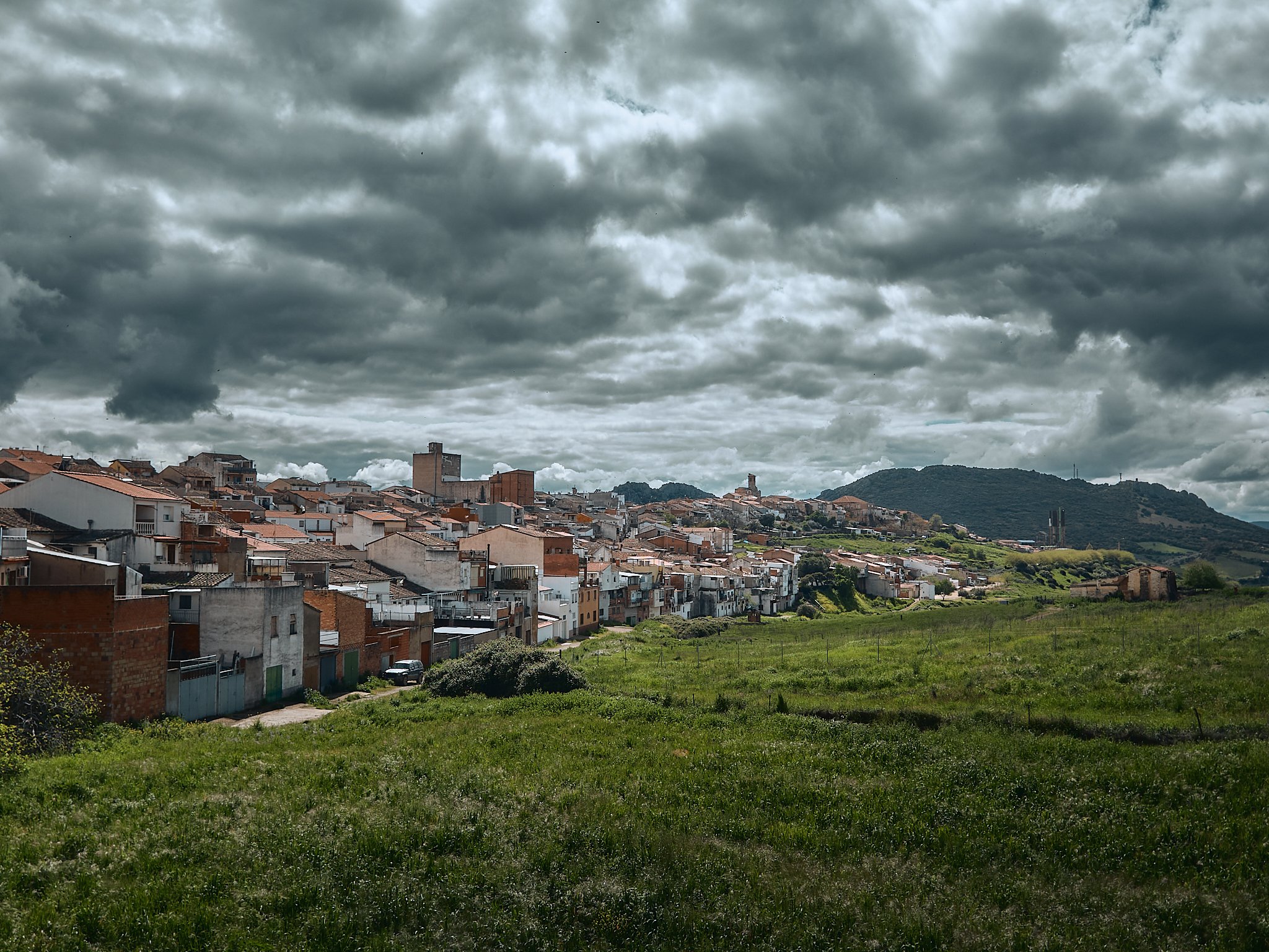 Vista de una ciudad en colina con casas y edificios de colores, sobre un campo verde y un cielo nublado.