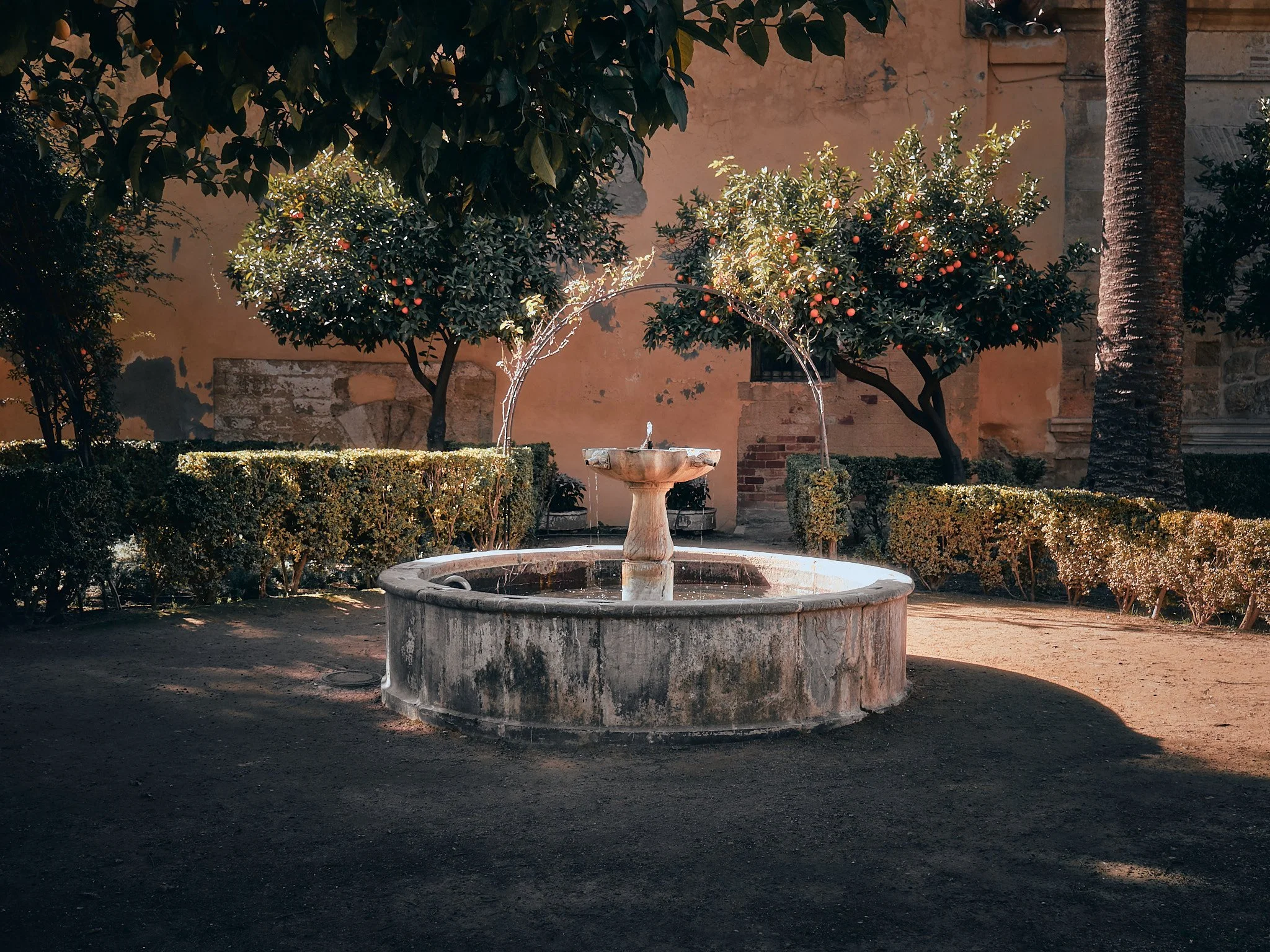 Fuente de piedra en un jardín con arbustos y árboles con frutos