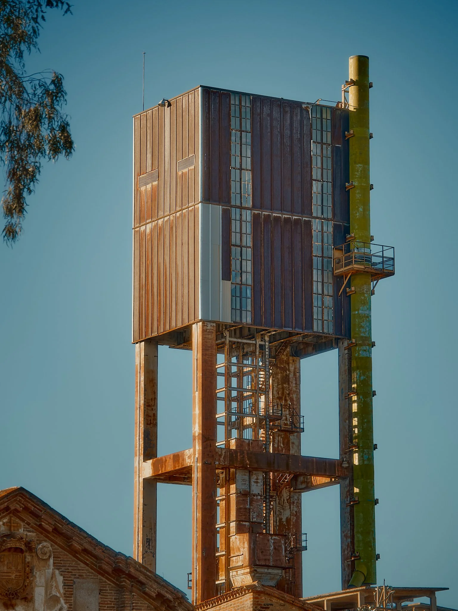 Estructura industrial oxidada con un tanque y tuberías en un cielo despejado.