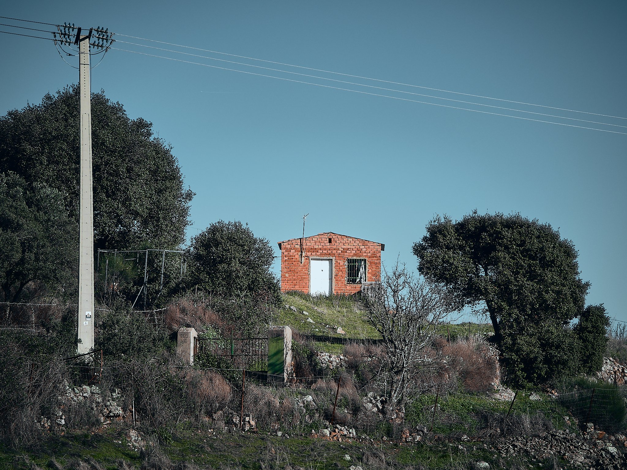 Casa pequeña de ladrillo en un paisaje rural con árboles y cielo despejado.