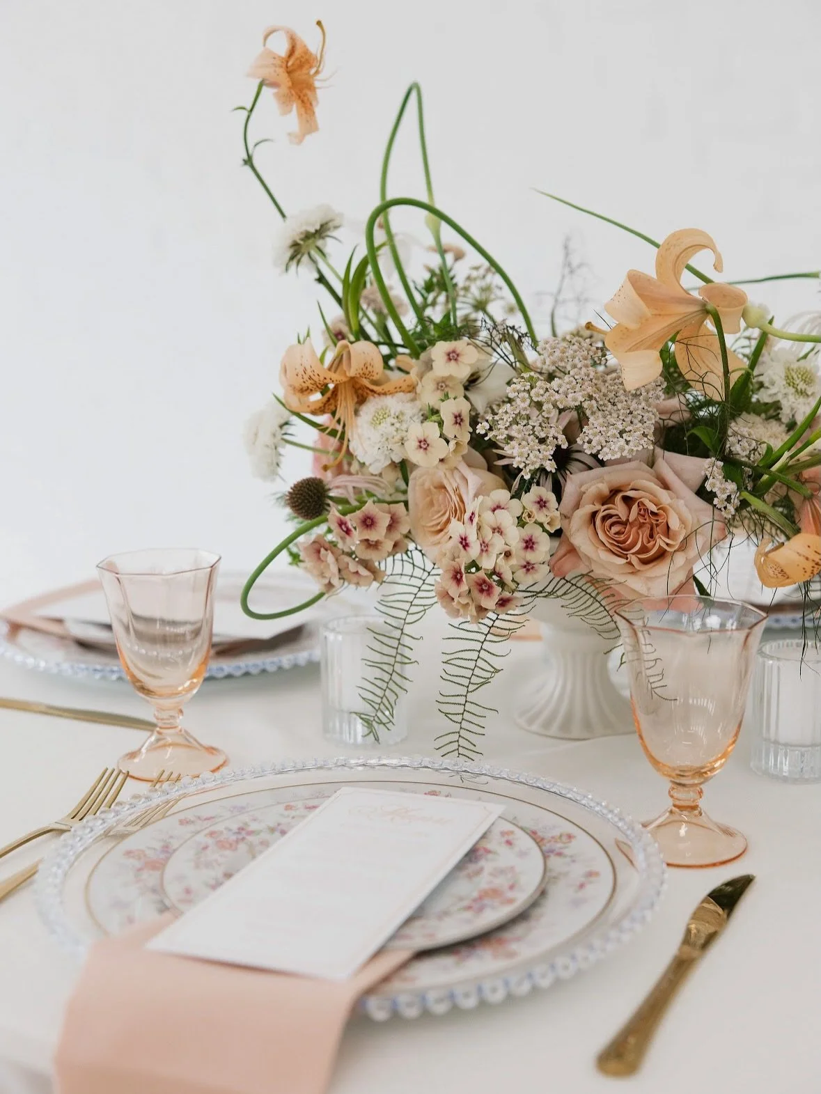A closer look at the table details!

Peach glassware, vintage-inspired china, gold flatware, and a garden-style arrangement with movement and gesture to keep it feeling natural and alive.

@brandingbyelizabeth 
@loganplanningsolutions 
@katietavarese