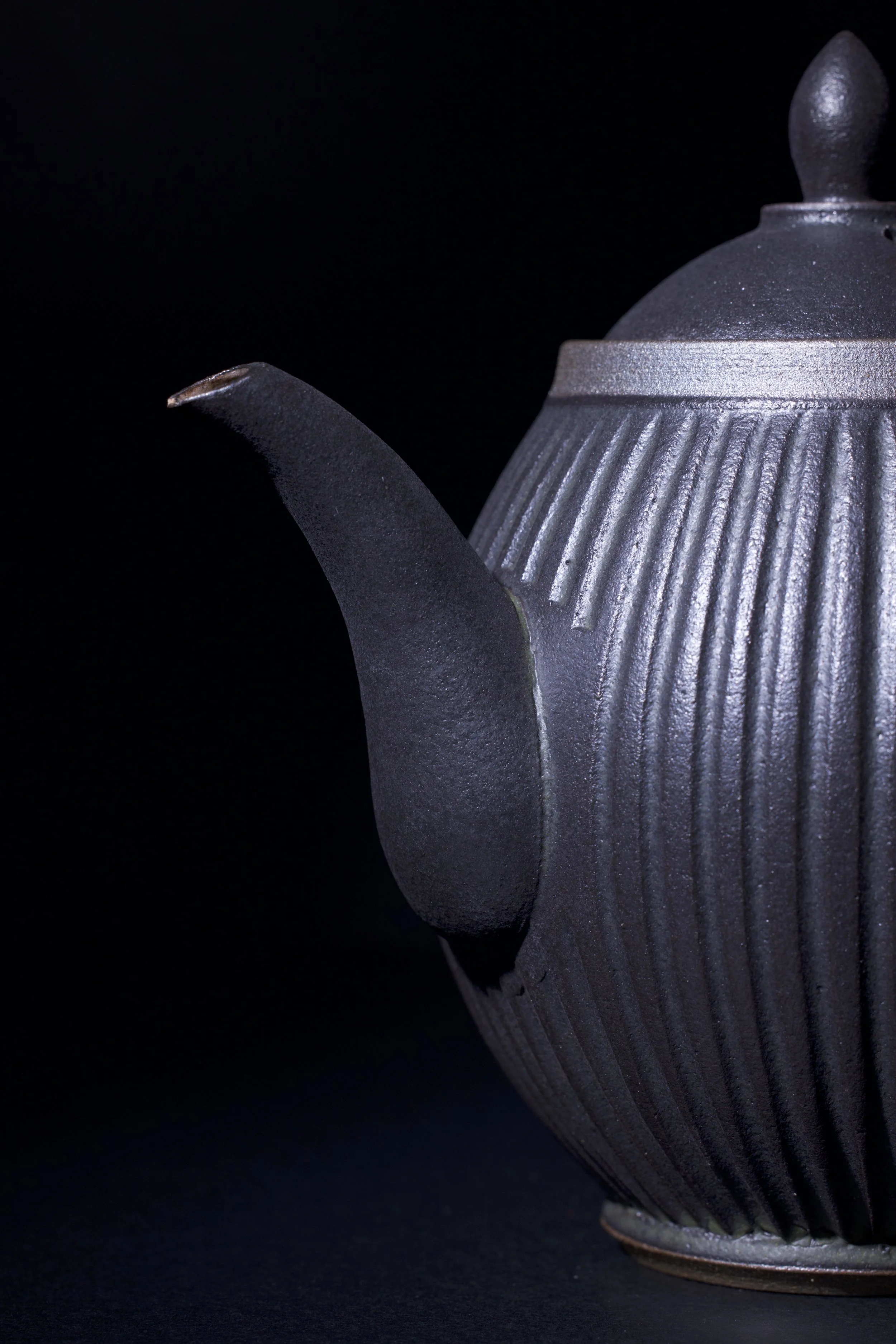 Close-up of a dark gray matte ceramic teapot with a textured ribbed surface, set against a black background.
