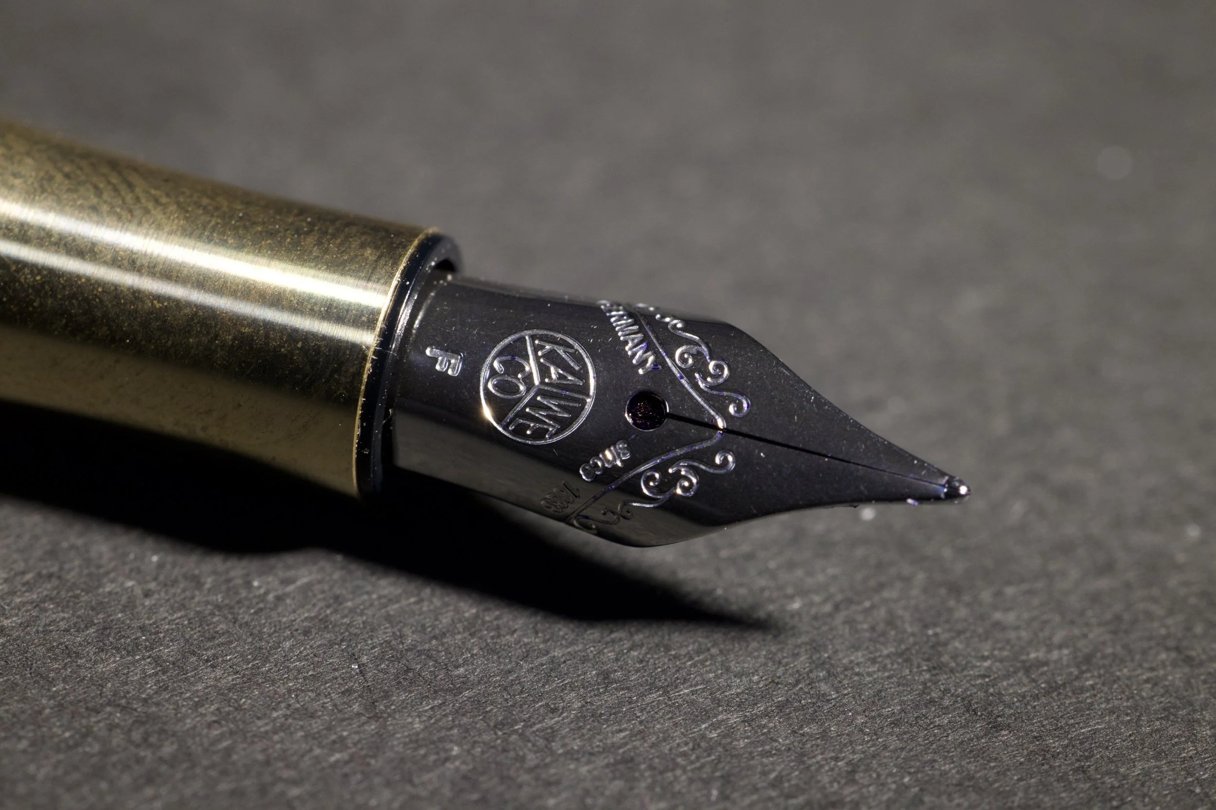 Close-up of a black and gold fountain pen nib resting on a dark grey surface.
