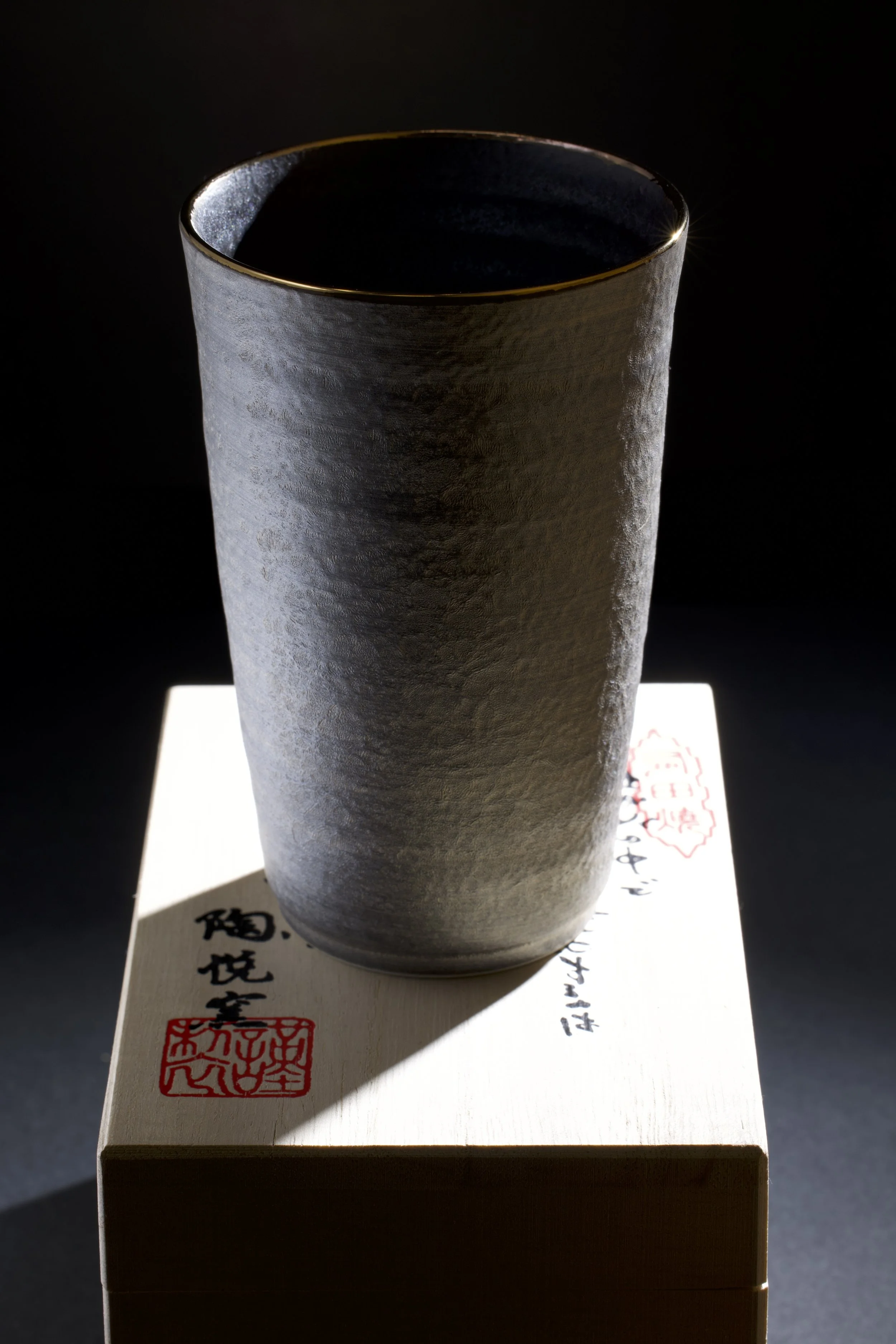 Close-up of a dark gray matte ceramic teapot with a textured ribbed surface, set against a black background.