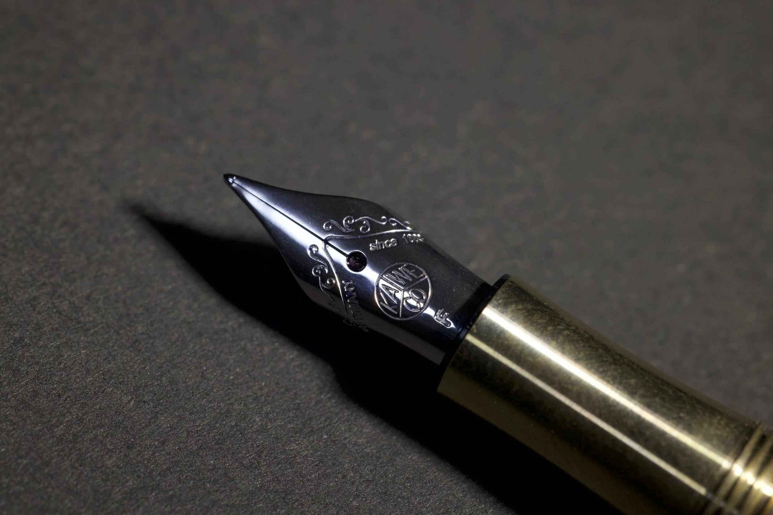 Close-up of a fountain pen with a black and gold body resting on a dark surface, casting a shadow.