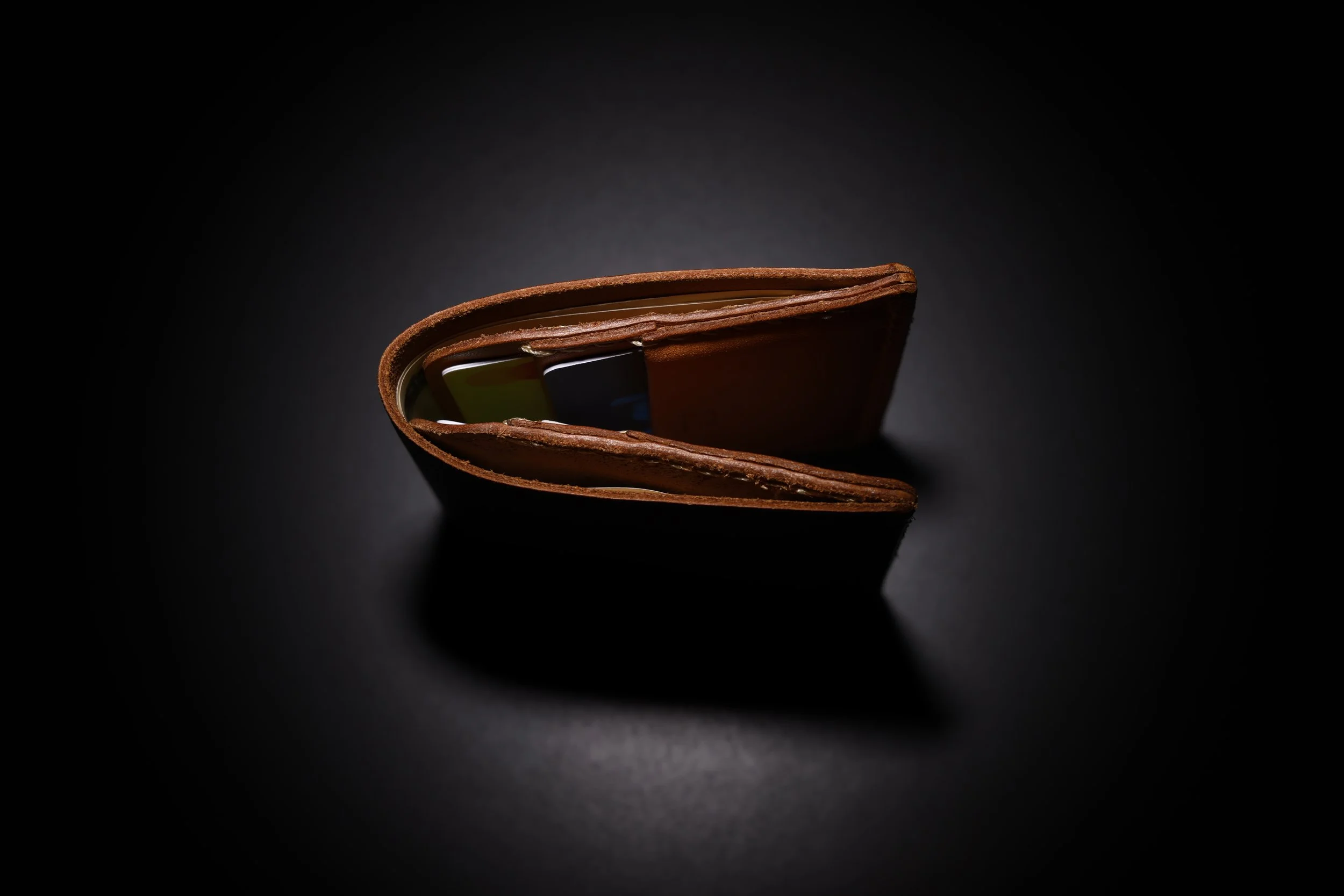 Open brown leather wallet with credit cards inside on a black background.