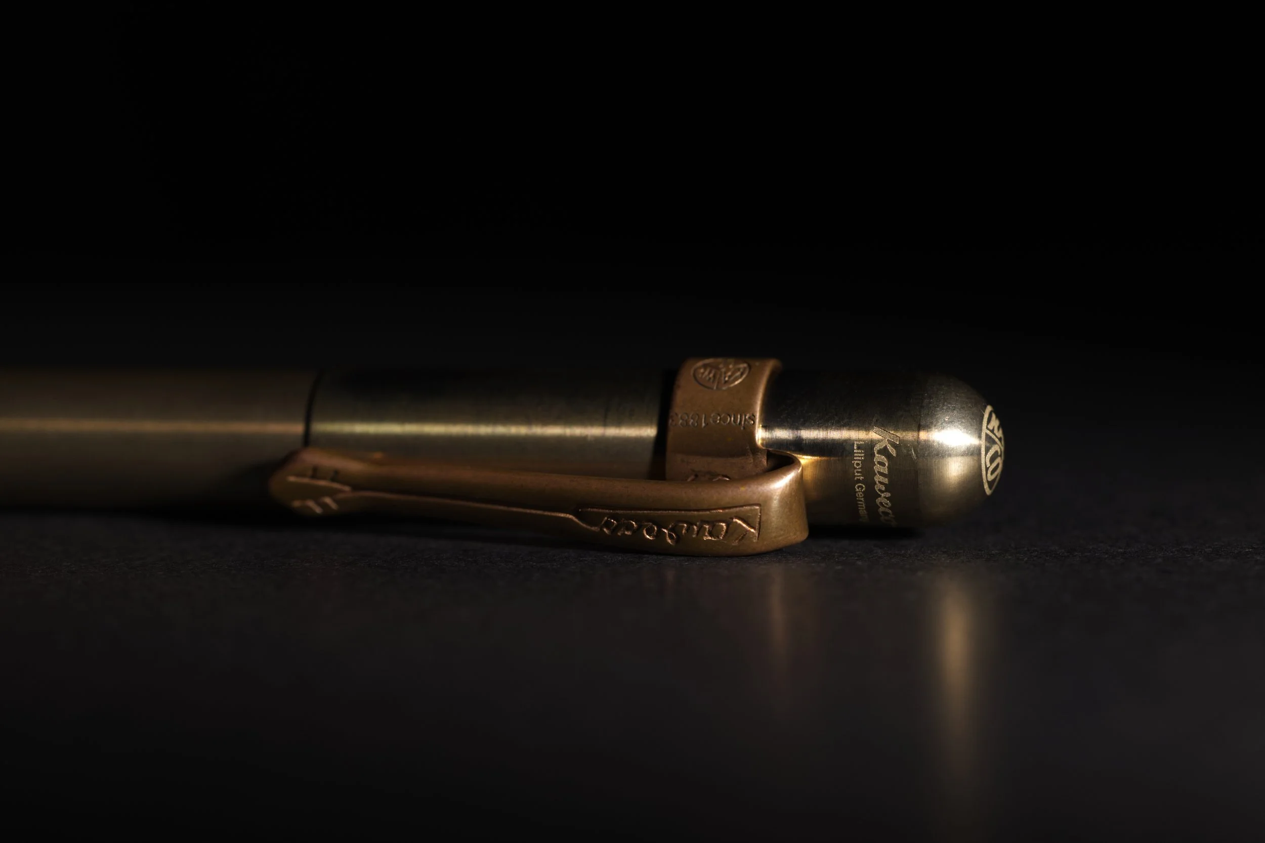 A vintage fountain pen with a gold clip and cap lies horizontally on a dark surface with dim lighting.