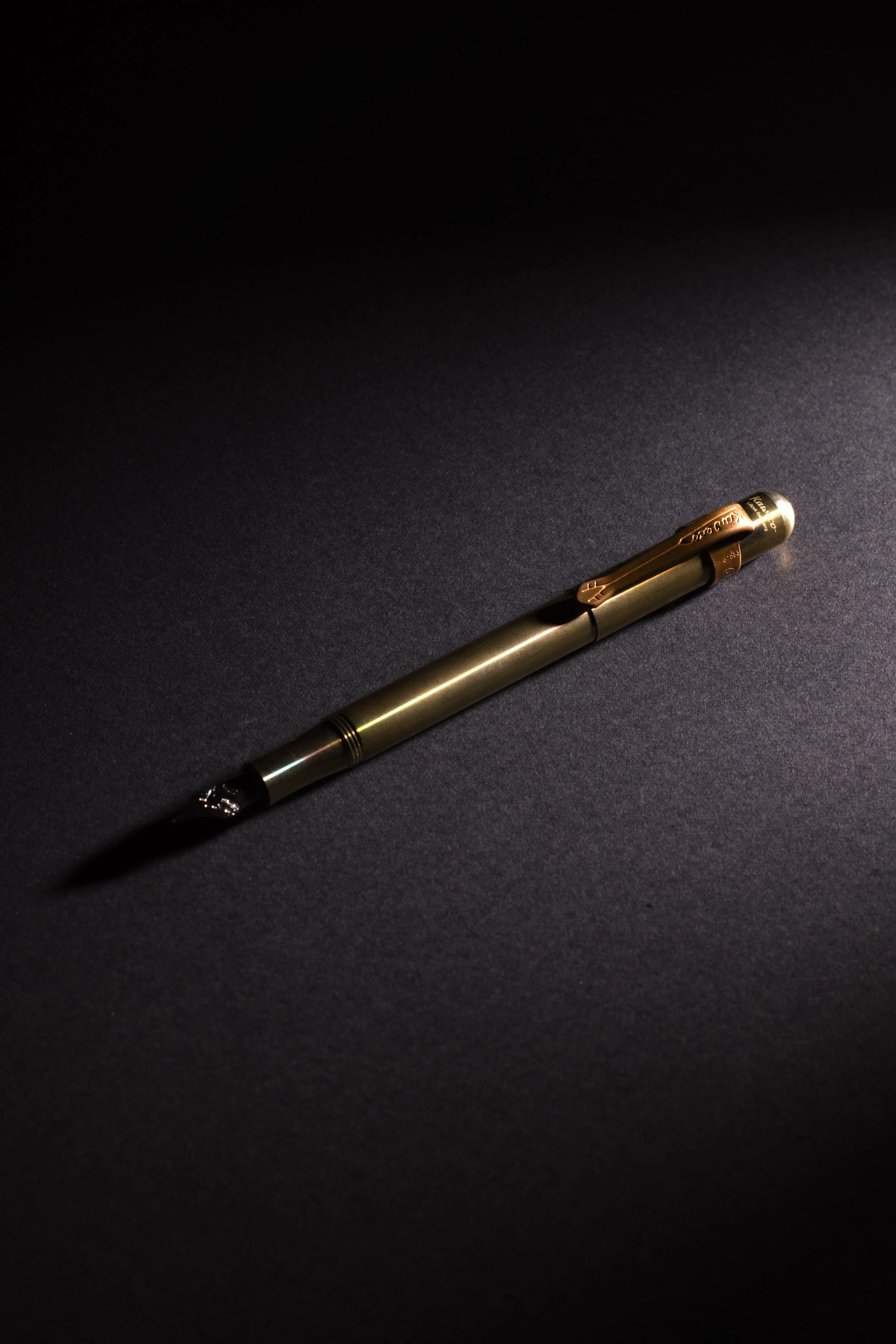 Metallic pen with a clip, lying on a dark surface with a light source highlighting its middle section.