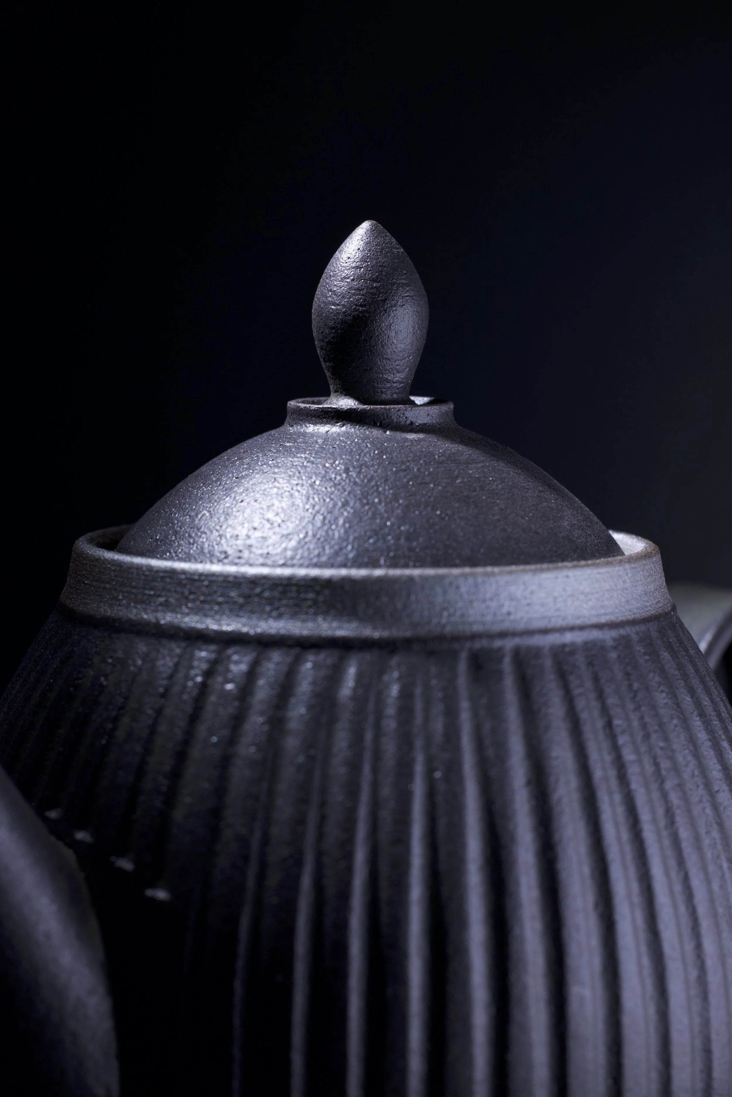 Close-up of a dark gray matte ceramic teapot with a textured ribbed surface, set against a black background.