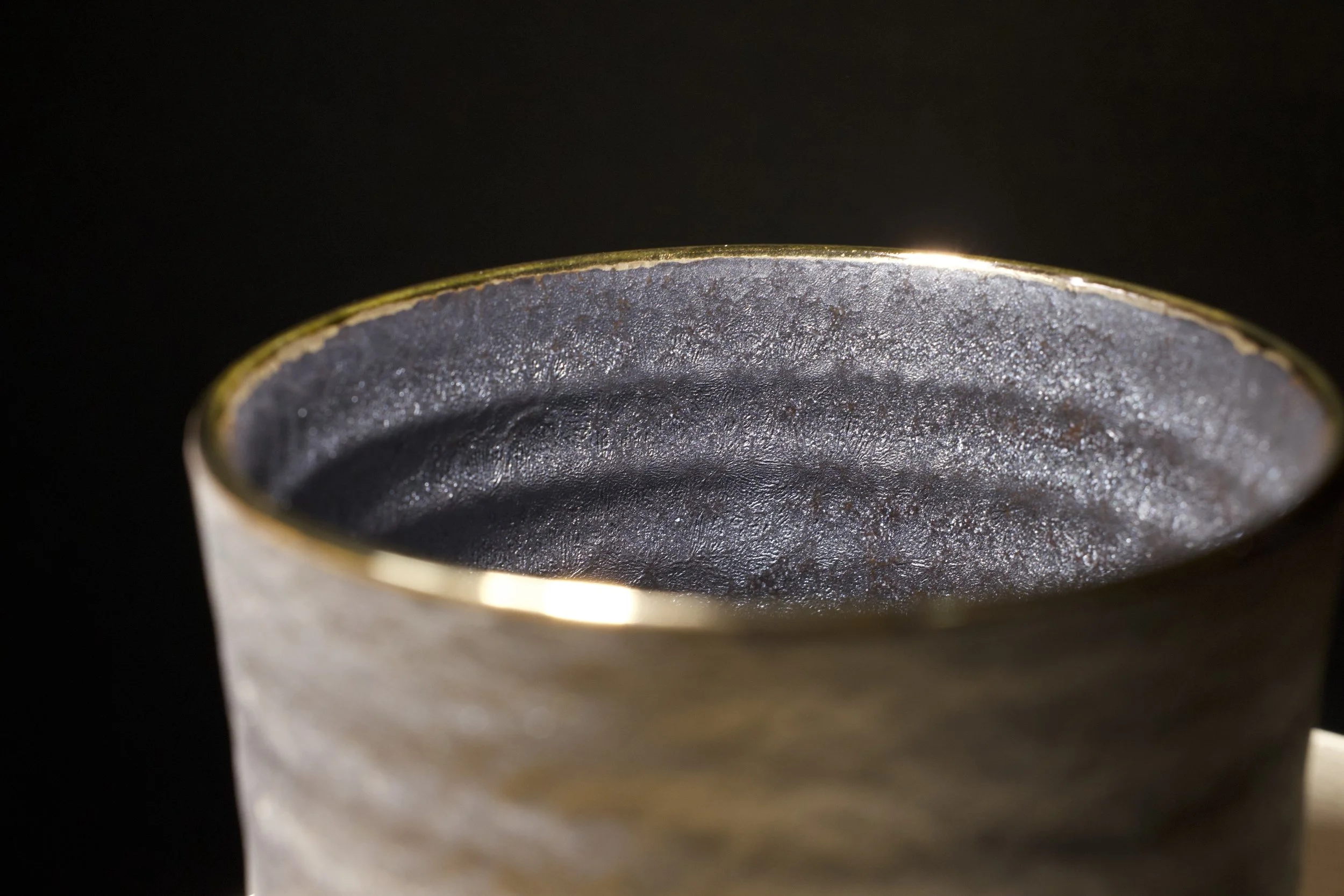 Close-up of a dark gray matte ceramic teapot with a textured ribbed surface, set against a black background.