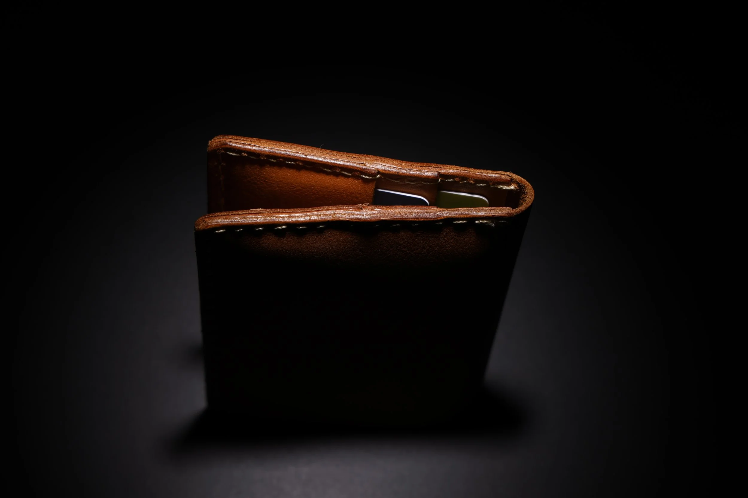 A brown leather wallet with a partially visible card inside, photographed against a black background with focused lighting.