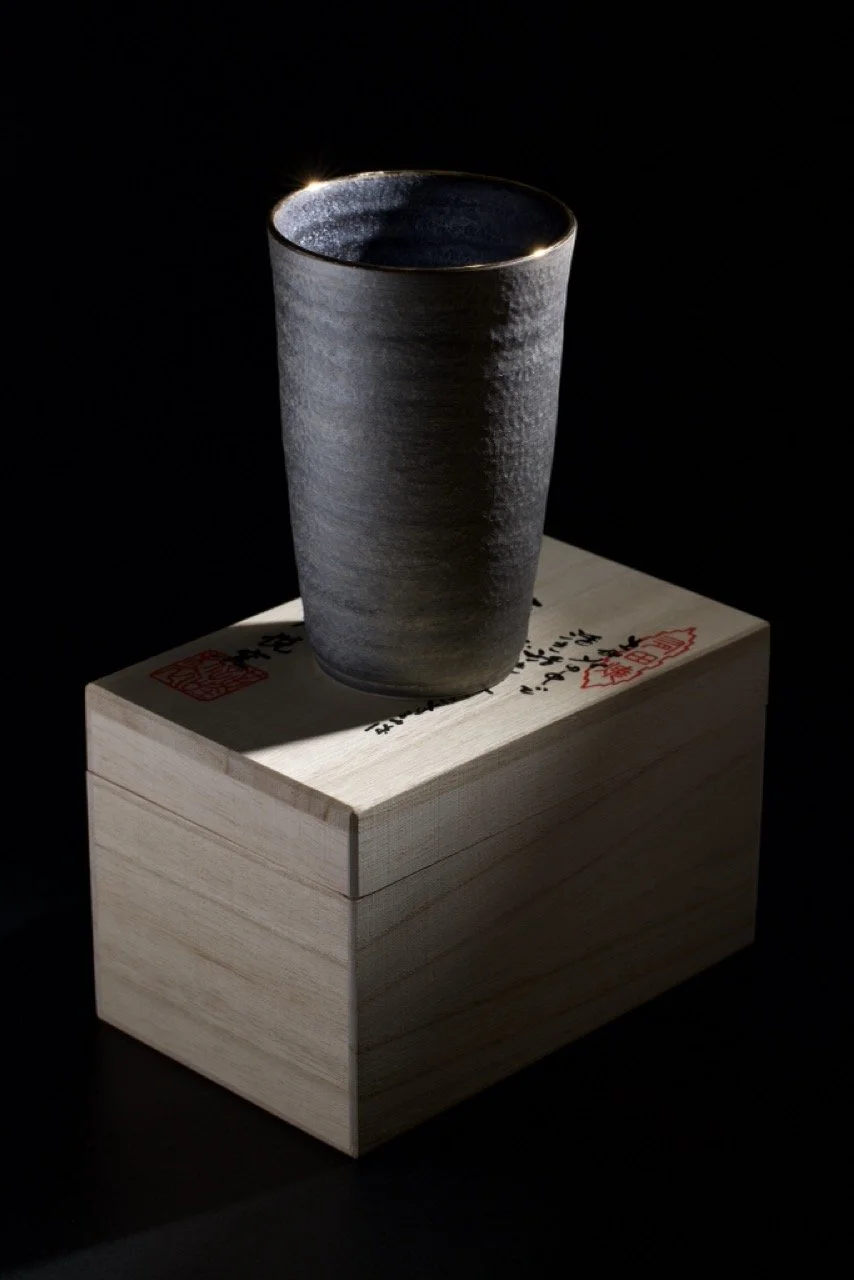 Close-up of a dark gray matte ceramic teapot with a textured ribbed surface, set against a black background.