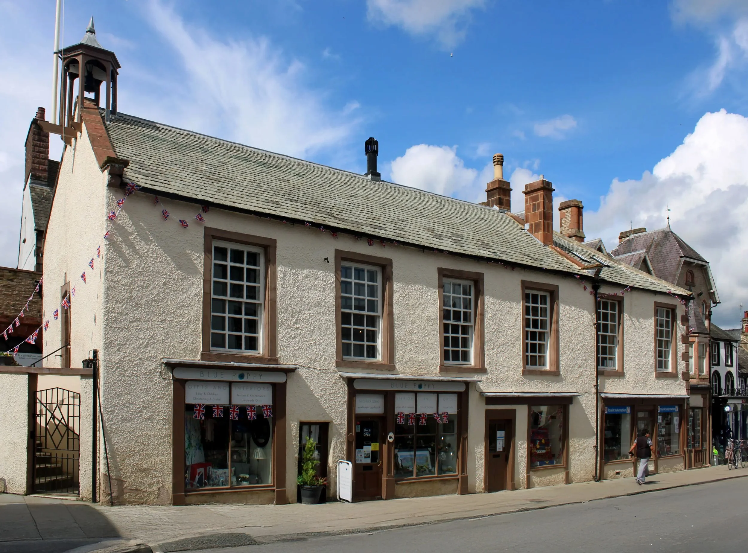 Moot Hall, Appleby-in-Westmorland, featuring rustic architecture, multiple windows, a tiled roof, and a bell tower under a partly cloudy sky.