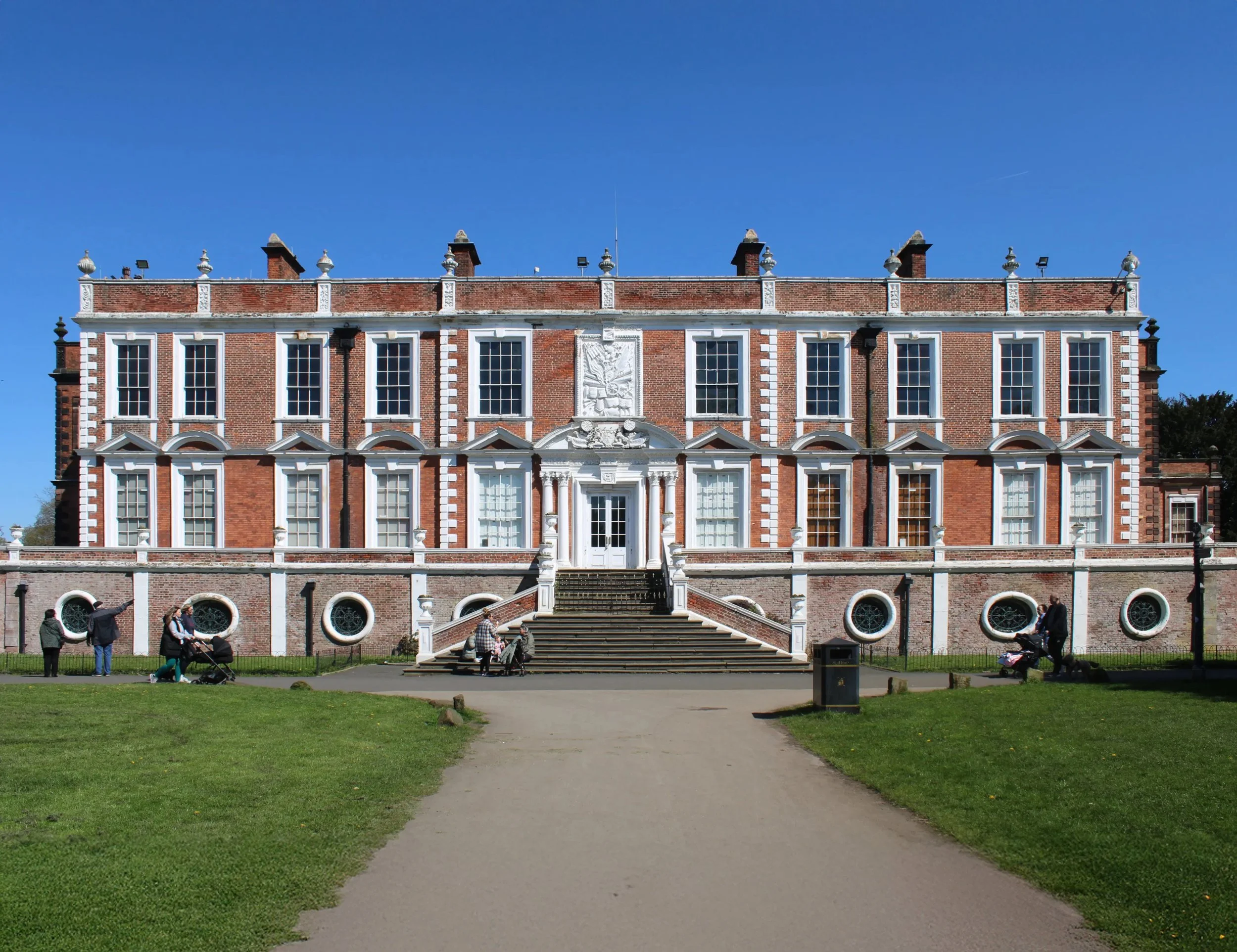 Croxteth Hall, Liverpool with white architectural details, long windows, and circular windows at ground level, set against a clear blue sky.