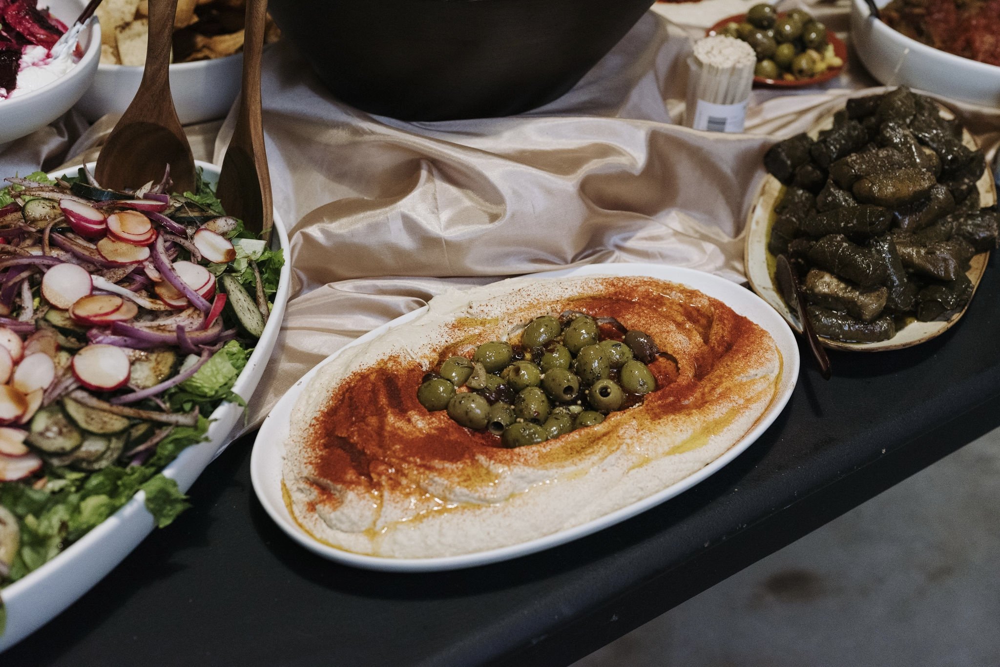 White plate of hummus with red paprika seasoning and gren olives in the center
