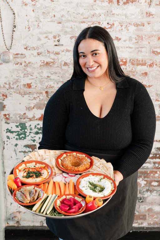 Chef Miranda holding silver tray filled with dips, veggies, and pickles