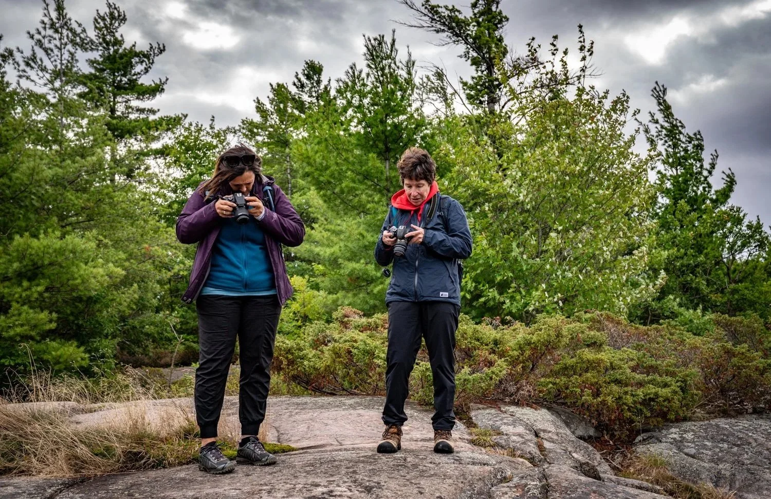 Two women standing with their cameras taking a landscape photo.
