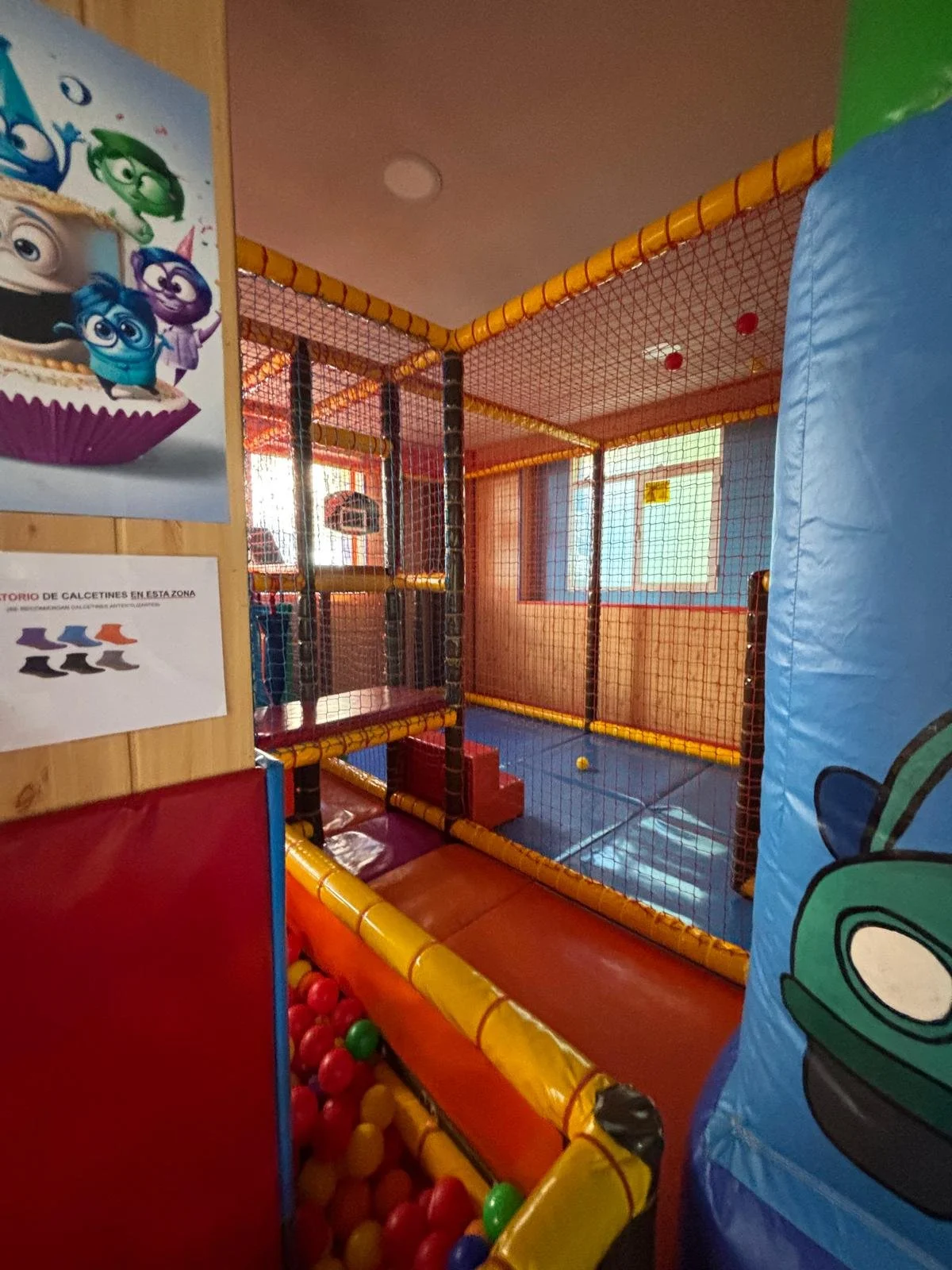 Área de juego cubierta para niños con colchonetas, redes y bolas de colores.