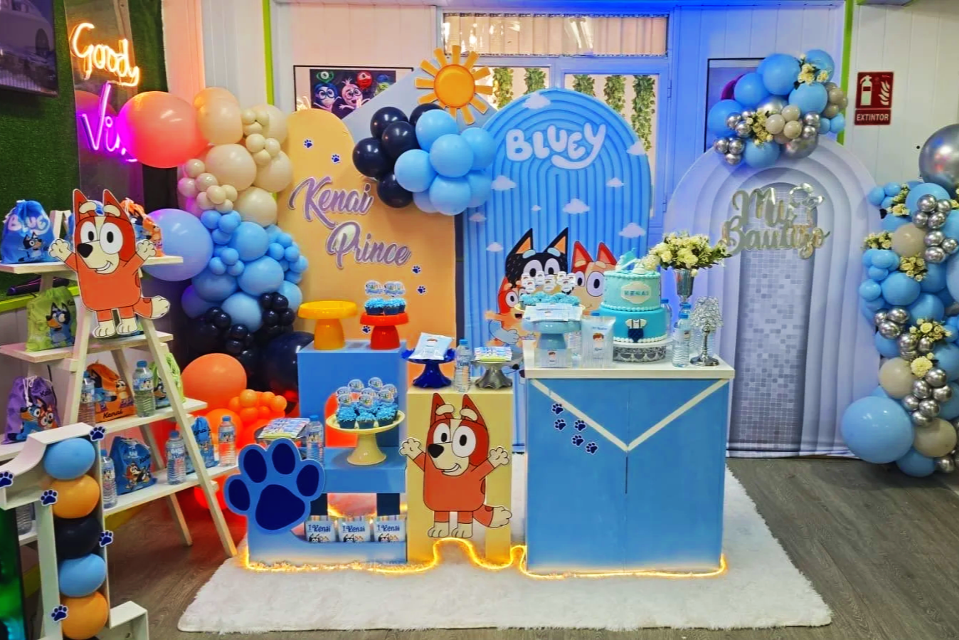 Decoración de fiesta infantil con tema de personajes de dibujos animados de perros y gatos, con globos de colores, tortas, y detalles en tonos azules, amarillo y blanco.