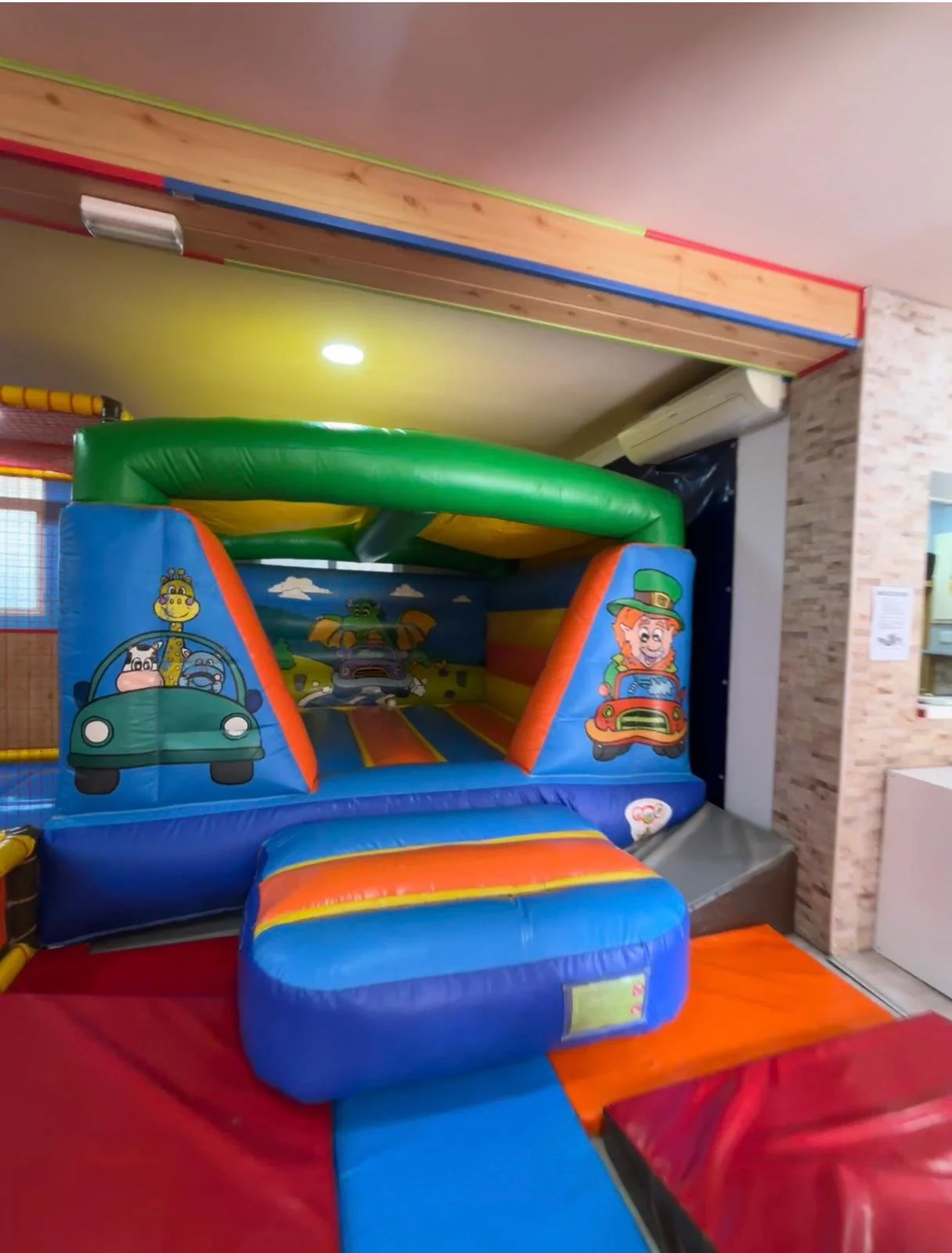 Castillo inflable infantil con personajes de dibujos animados en parque de juegos cubierto.