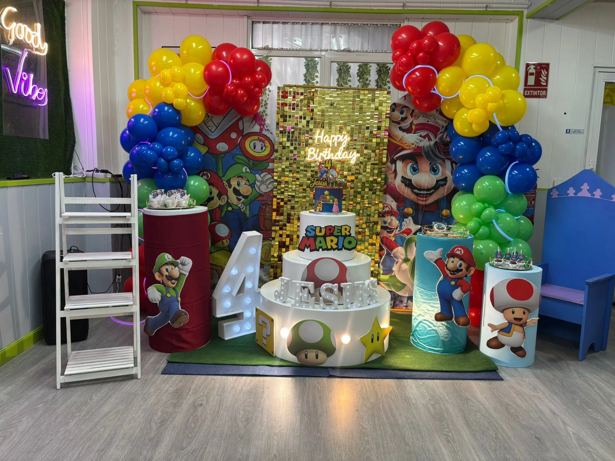 Decoración de fiesta de cumpleaños con temática de Super Mario, con globos de colores, figuras de personajes y un pastel en forma de hongo y estrella, en una habitación colorida.