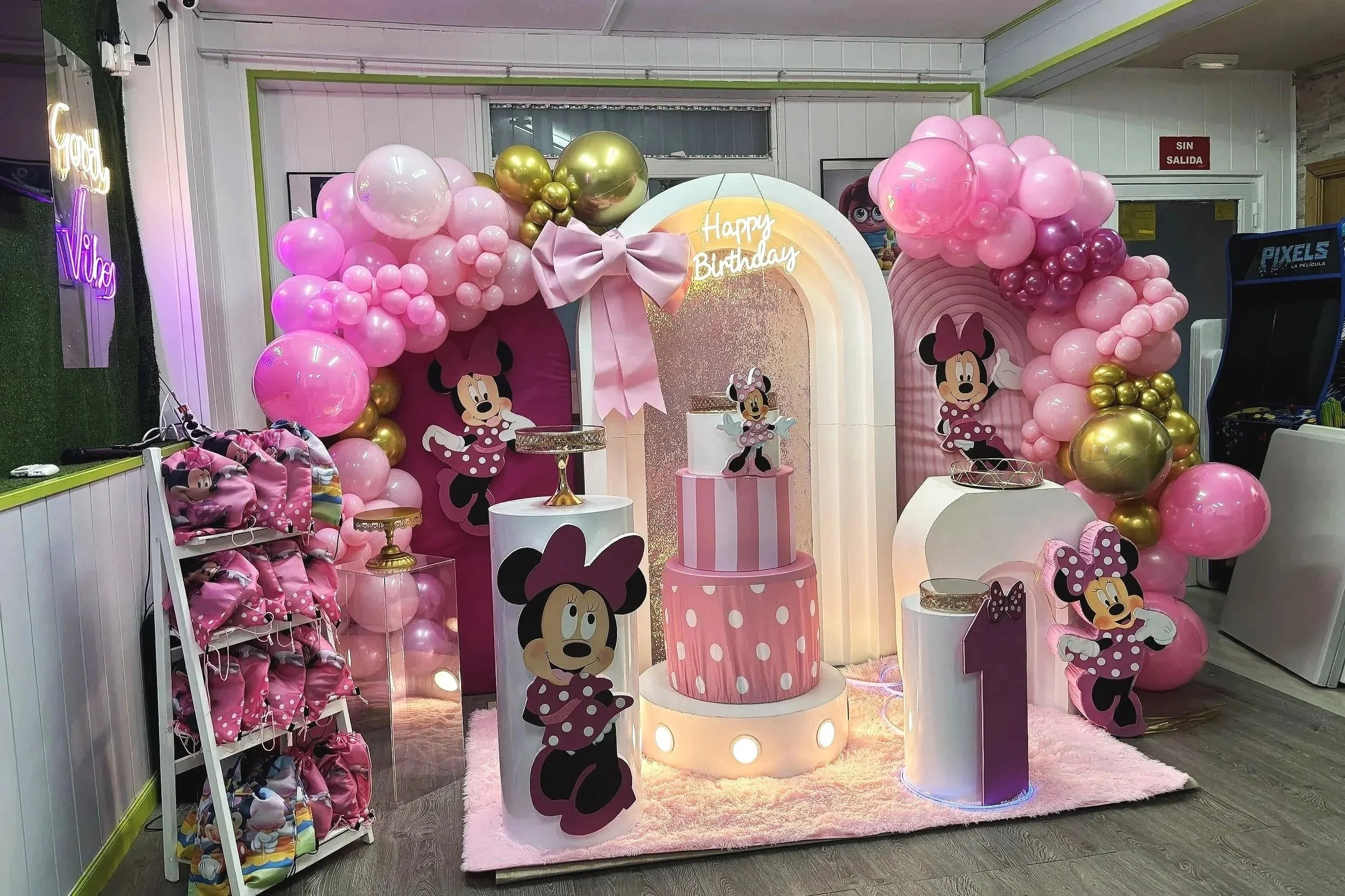 Decoración de fiesta de cumpleaños temática de Minnie Mouse con globos rosados y dorados, cartel que dice 'Happy Birthday', y figuras de Minnie Mouse decorativas.