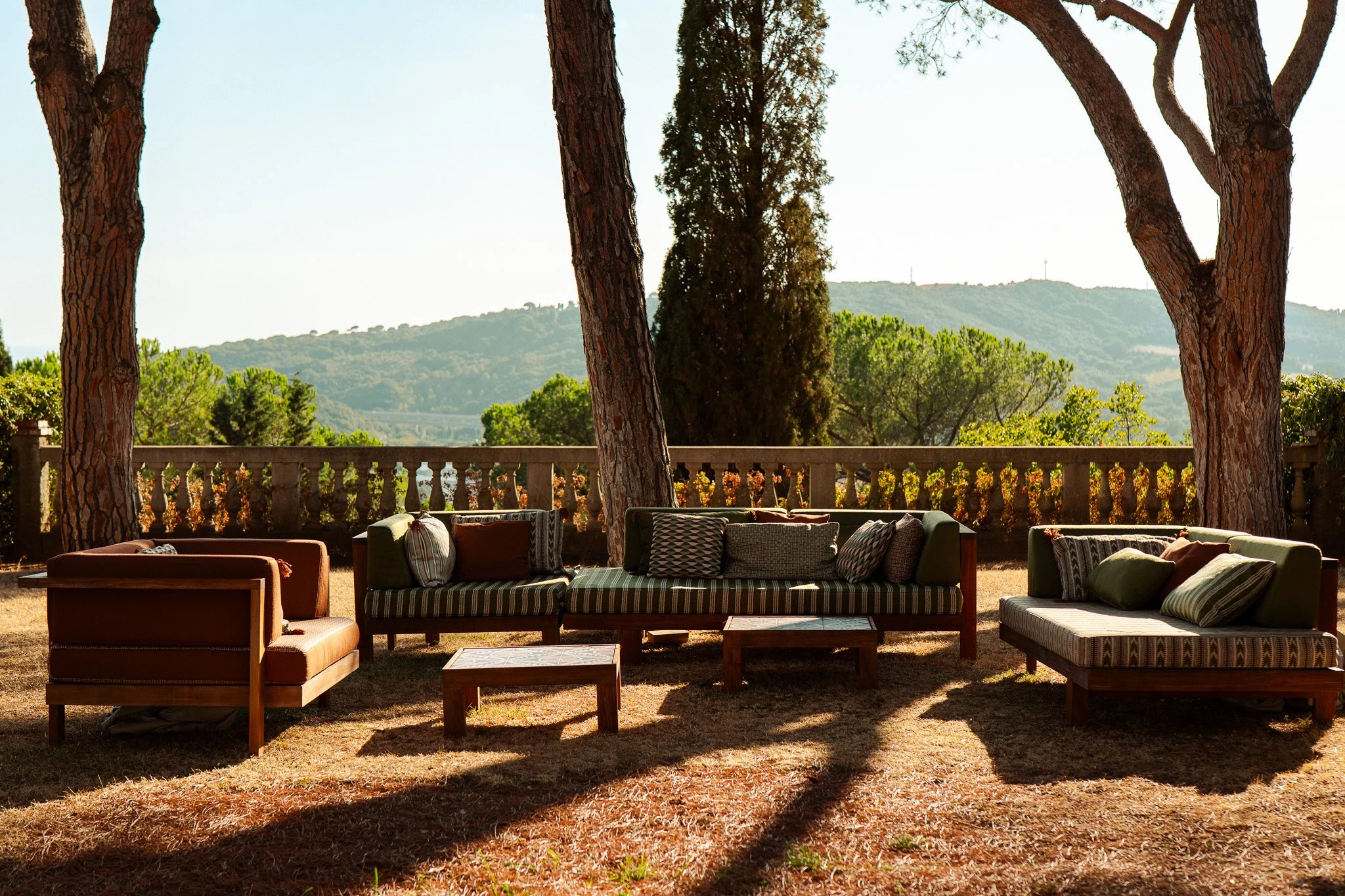 Outdoor seating area with three sofas and a coffee table, surrounded by trees and mountains in the background