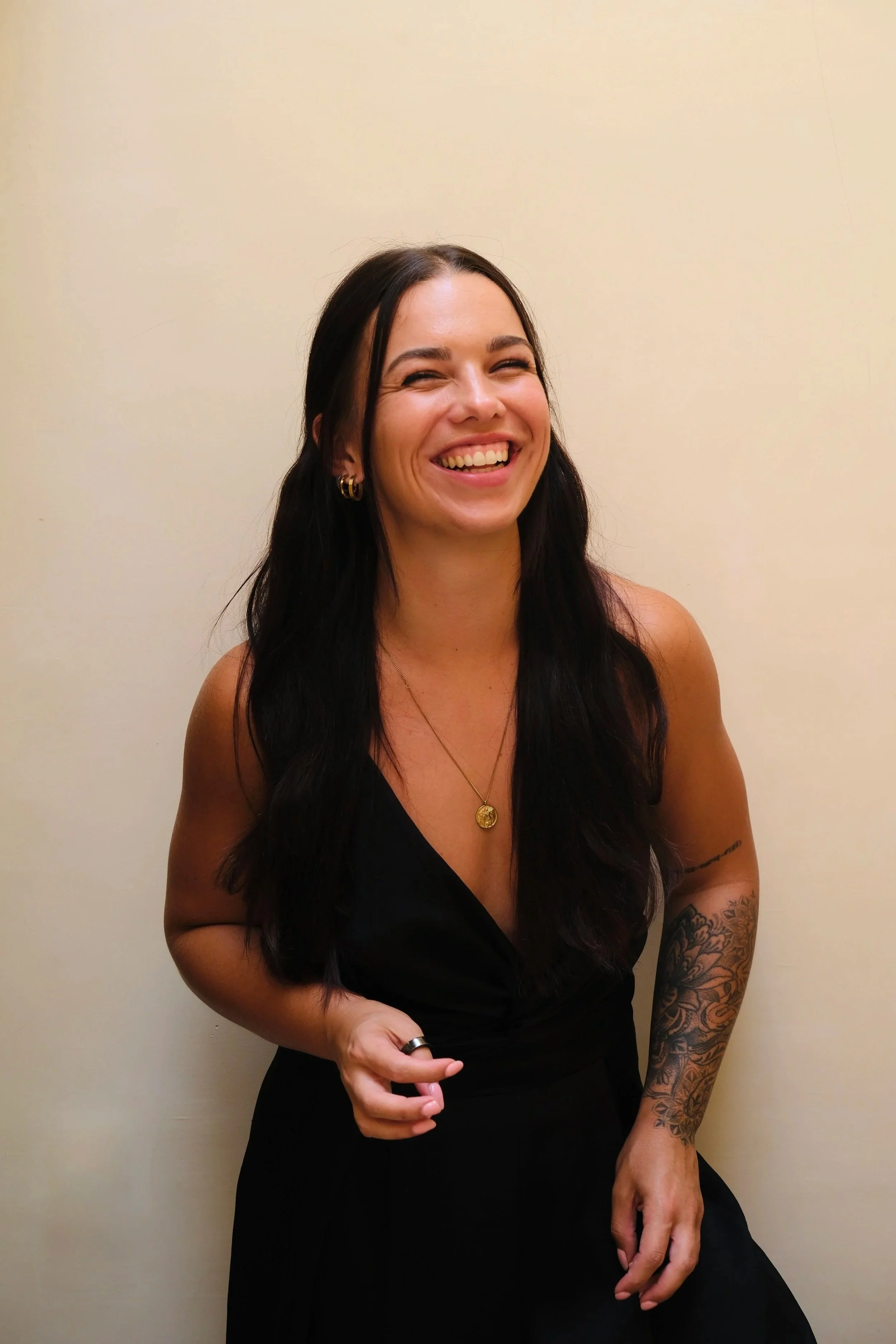 co-founder iris, long dark hair, black jumpsuit, beige background, smiling