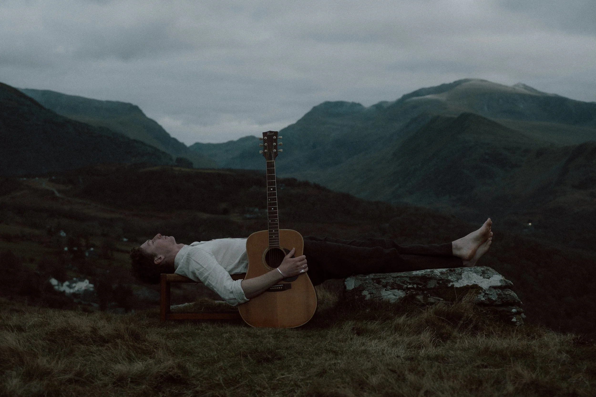man lying down with guitar with mountain views in the background