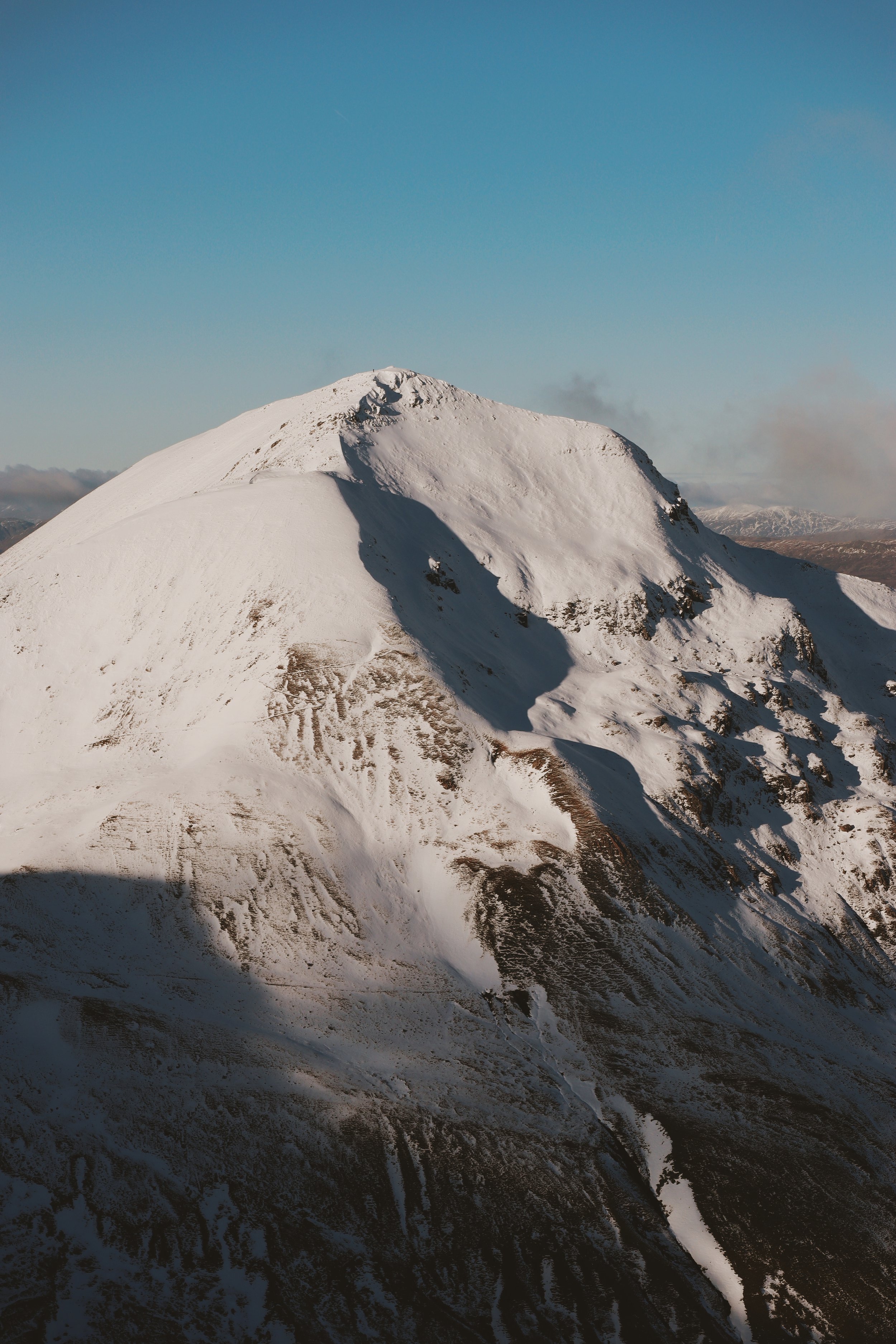 Snow-covered mountain under a clear blue sky with some clouds in the background.