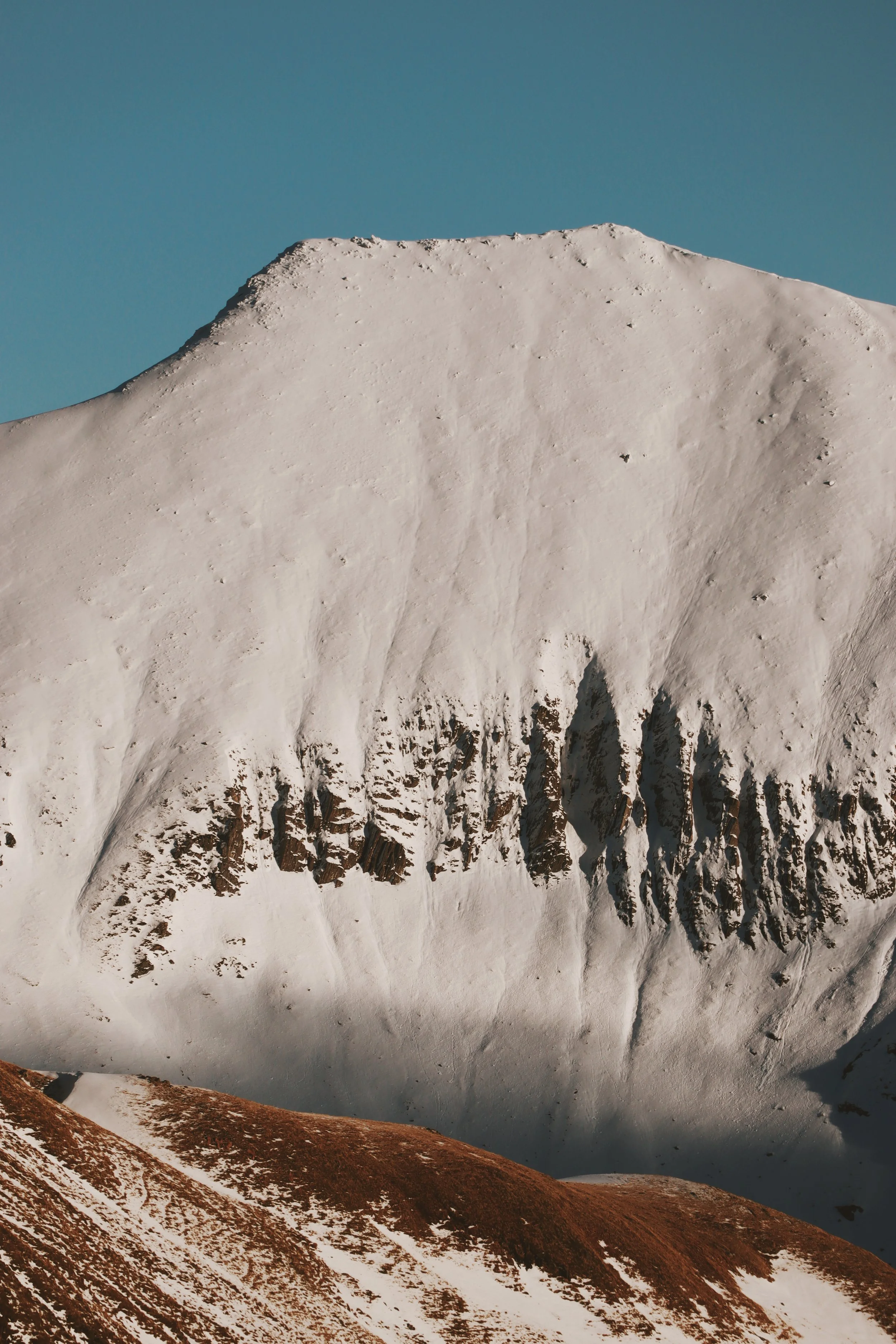 Snow-covered mountain with rugged rock formations and a clear blue sky.