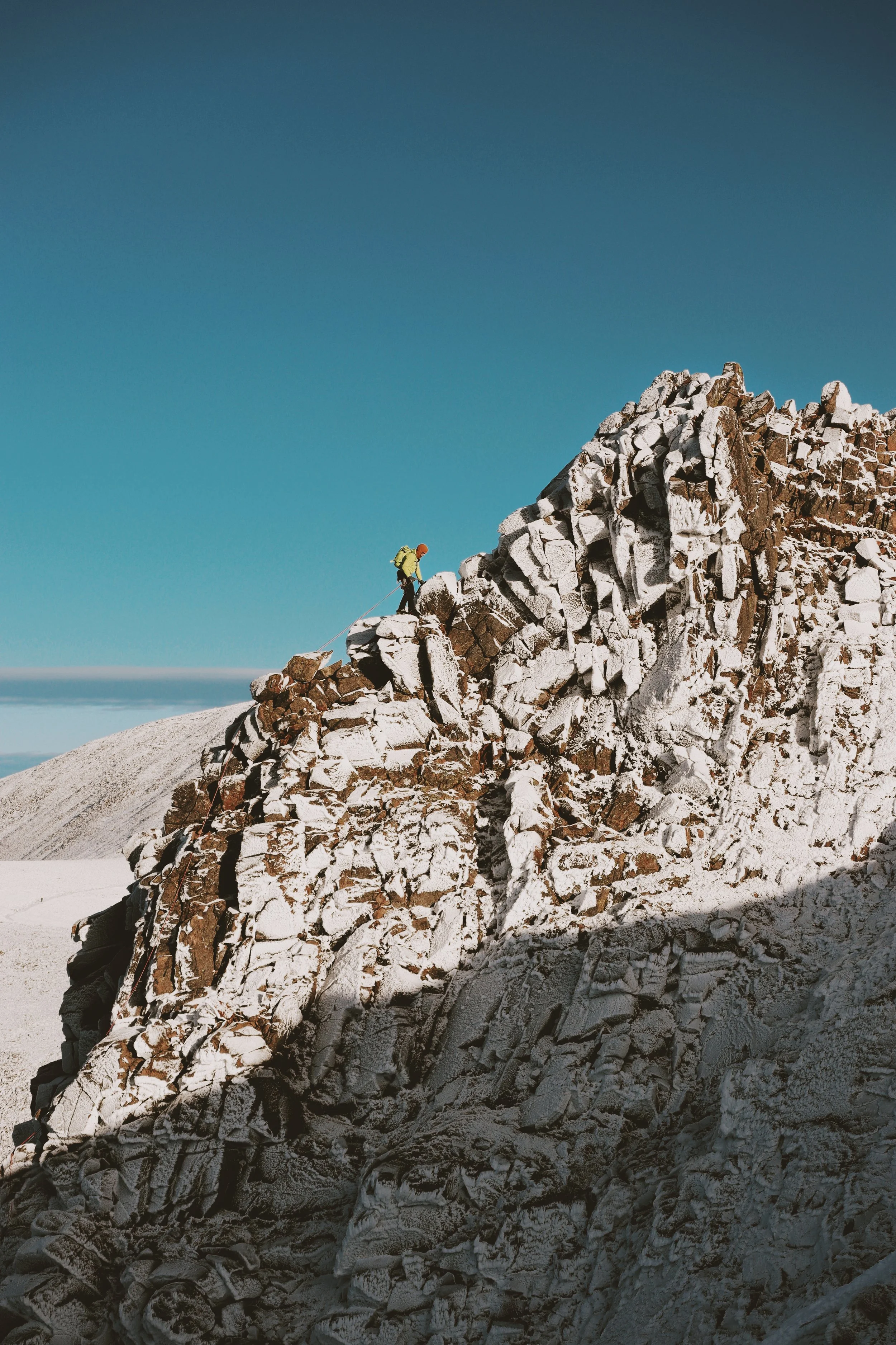 A person mountain climbing on a snow-covered rocky peak under a clear blue sky.