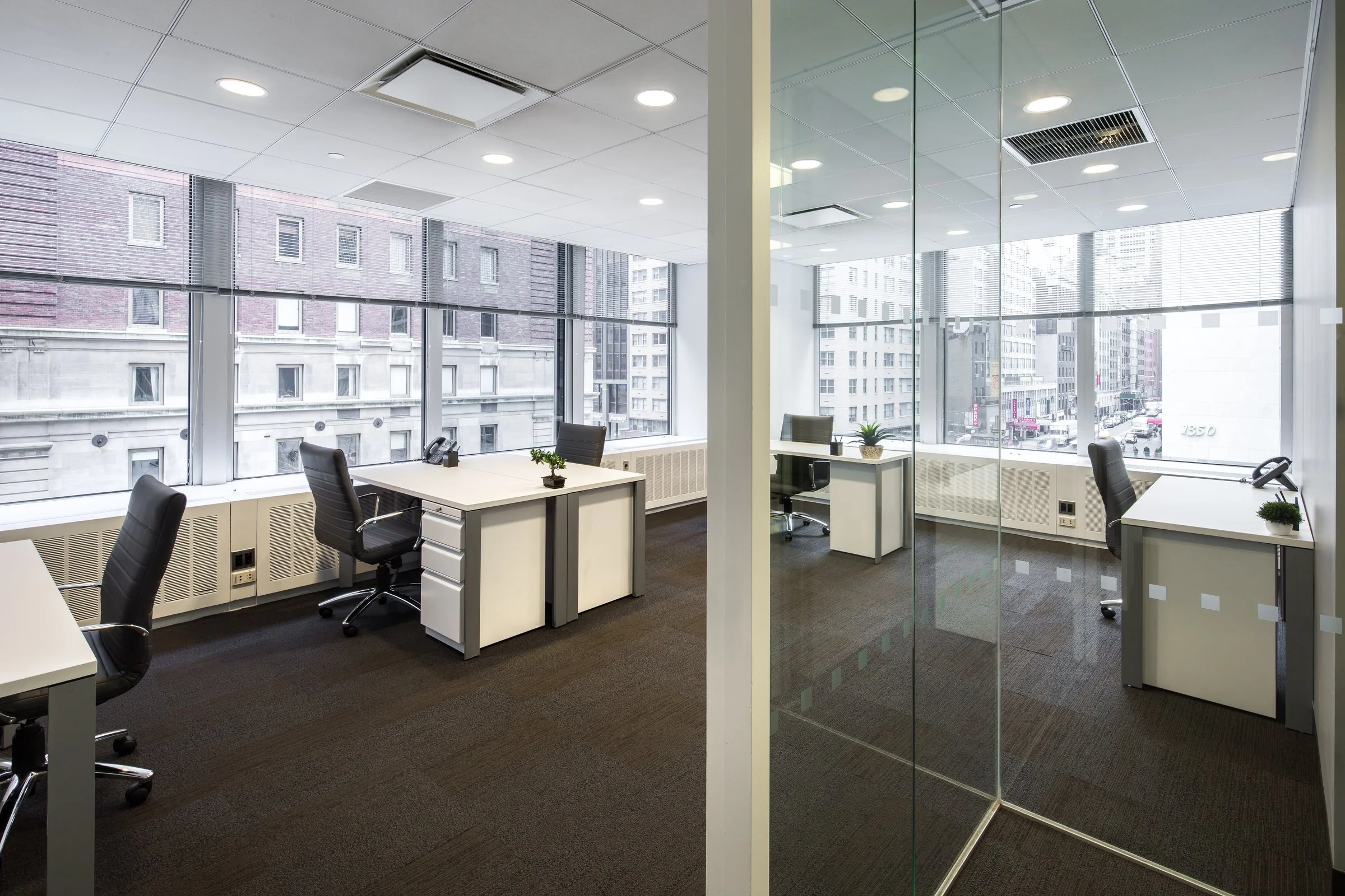 Furnished team office space for rent in Midtown Manhattan with glass walls, multiple desks, and corner city views