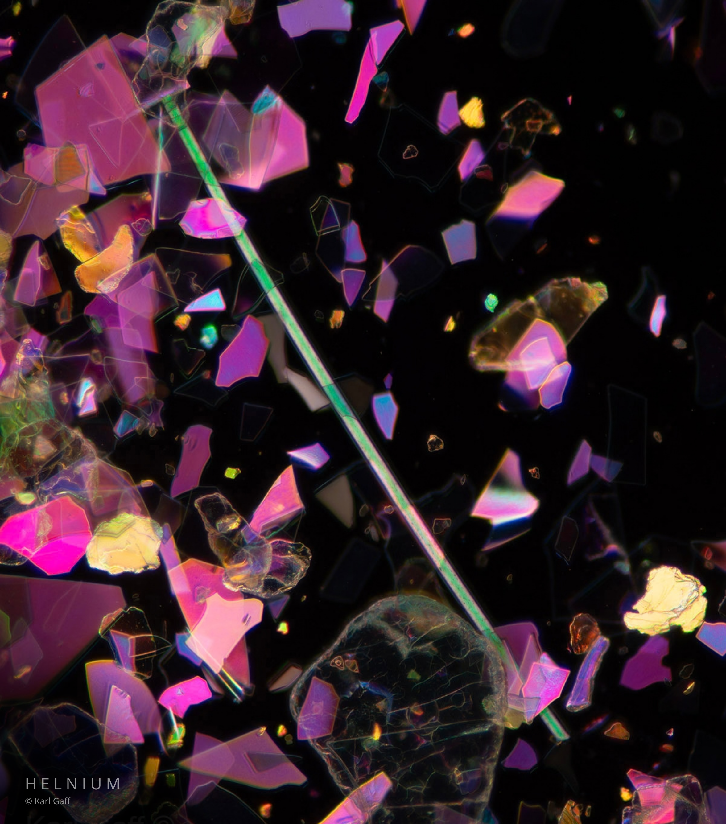 Lip gloss texture photographed under a microscope, showing microscopic cosmetic pigments and reflective material. Original Helnium scientific image.