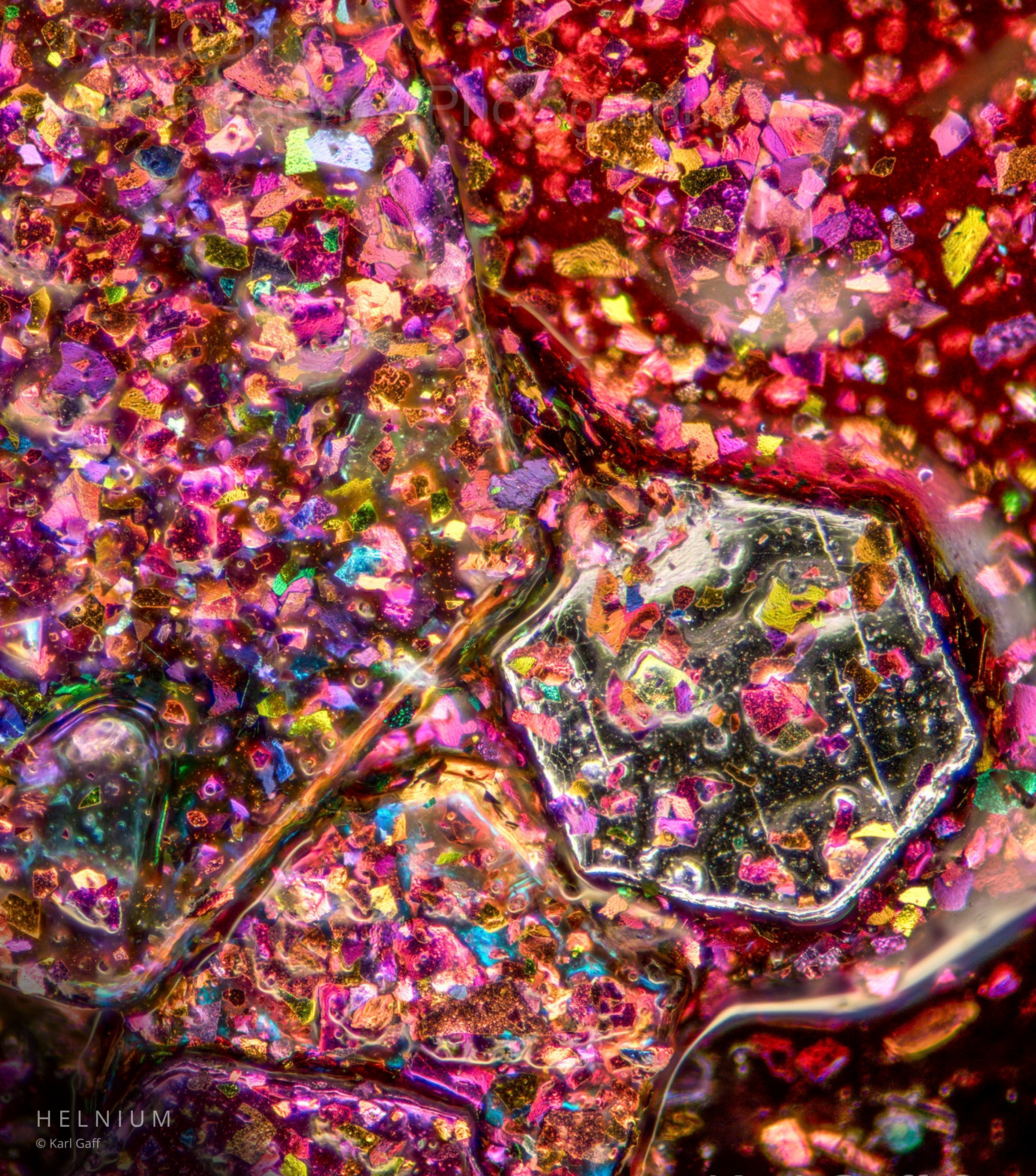 Prismatic glitter balm under the microscope, revealing colorful reflective particles and microscopic cosmetic texture. Helnium Scientific Design.