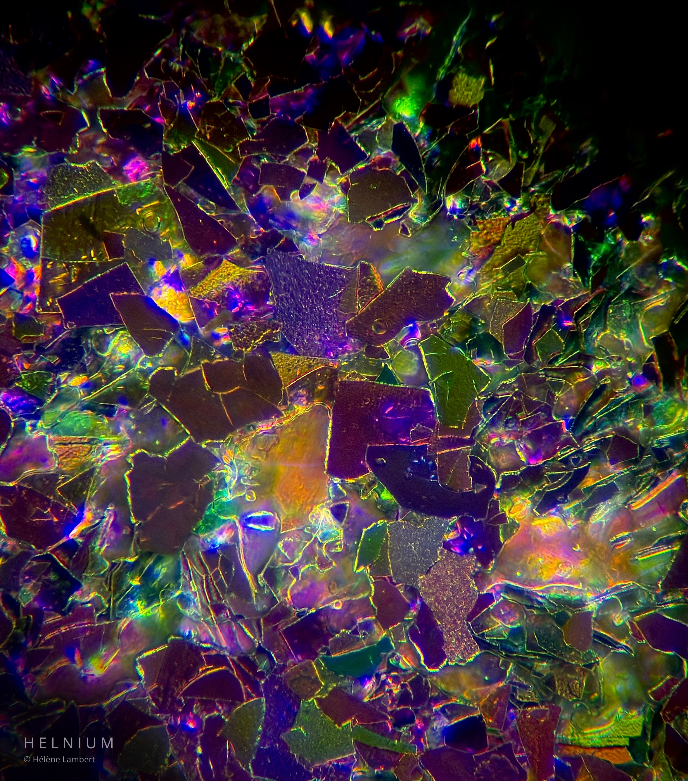 Galaxy eyeshadow pigment particles observed under a microscope, second micrograph showing reflective cosmetic structures. Helnium Scientific Design.